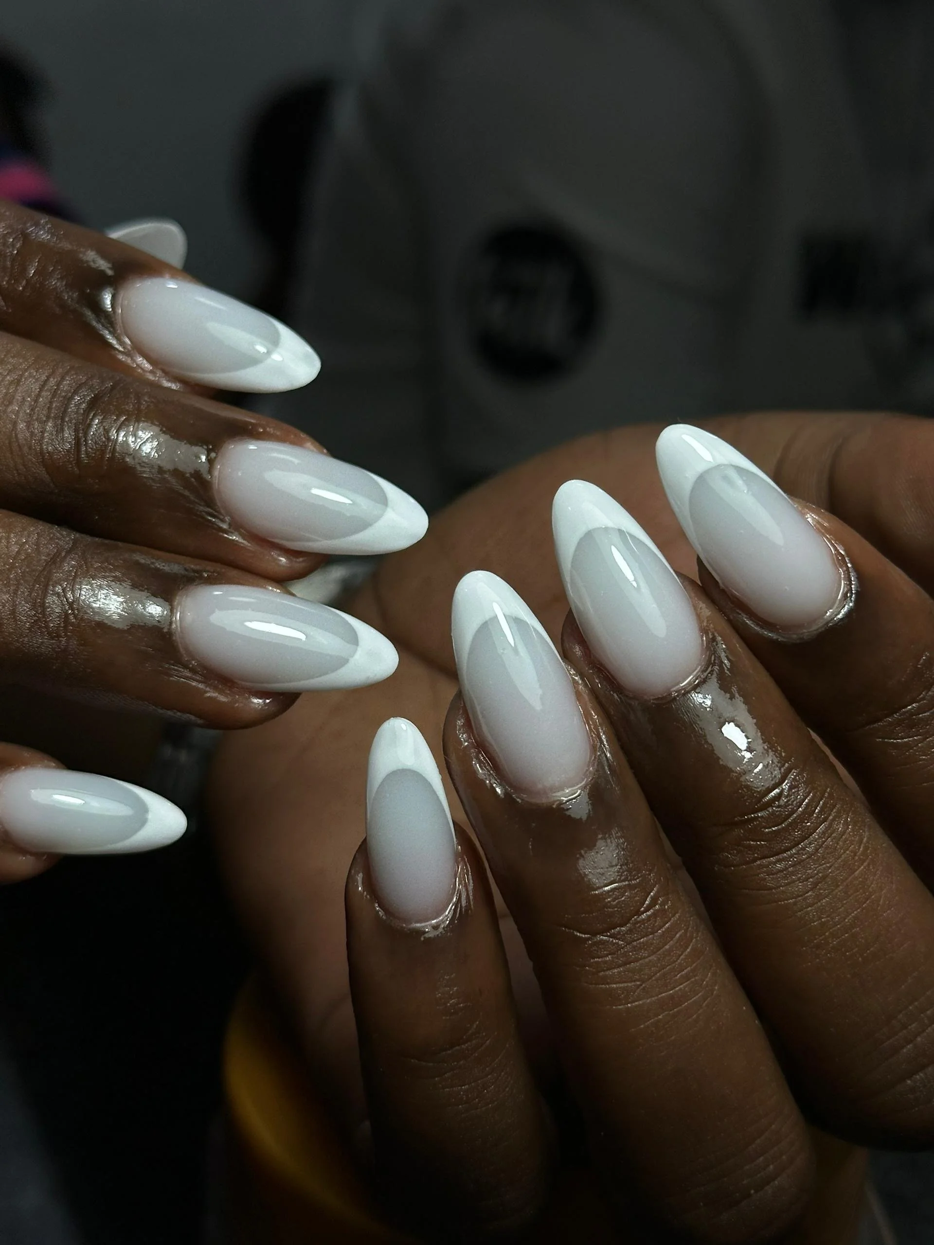 Close-up of a person's hands with freshly manicured white and gray gradient almond-shaped nails.