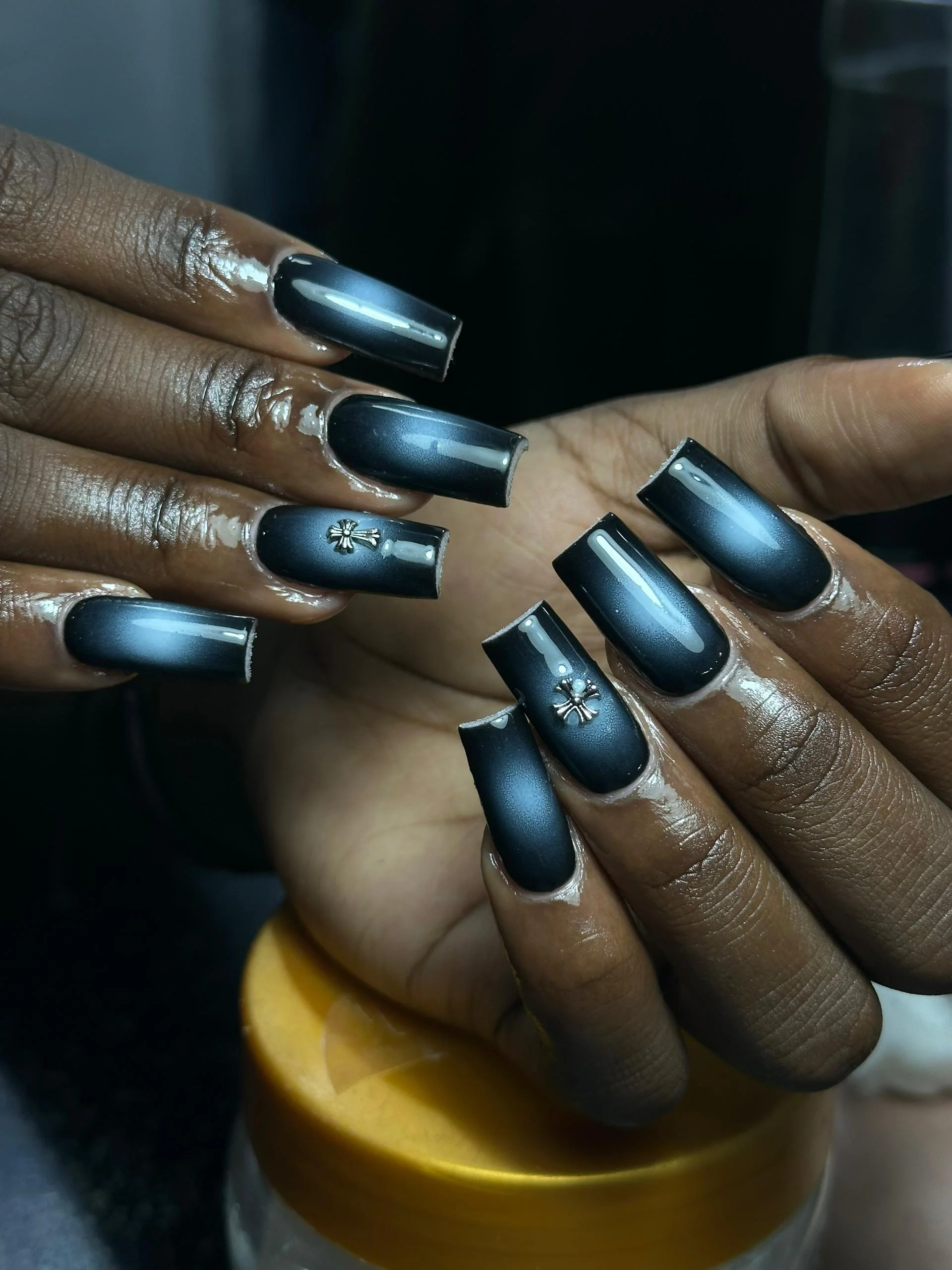 Close-up of hands with manicured nails painted in matte black with white streaks and small silver bee embellishments.