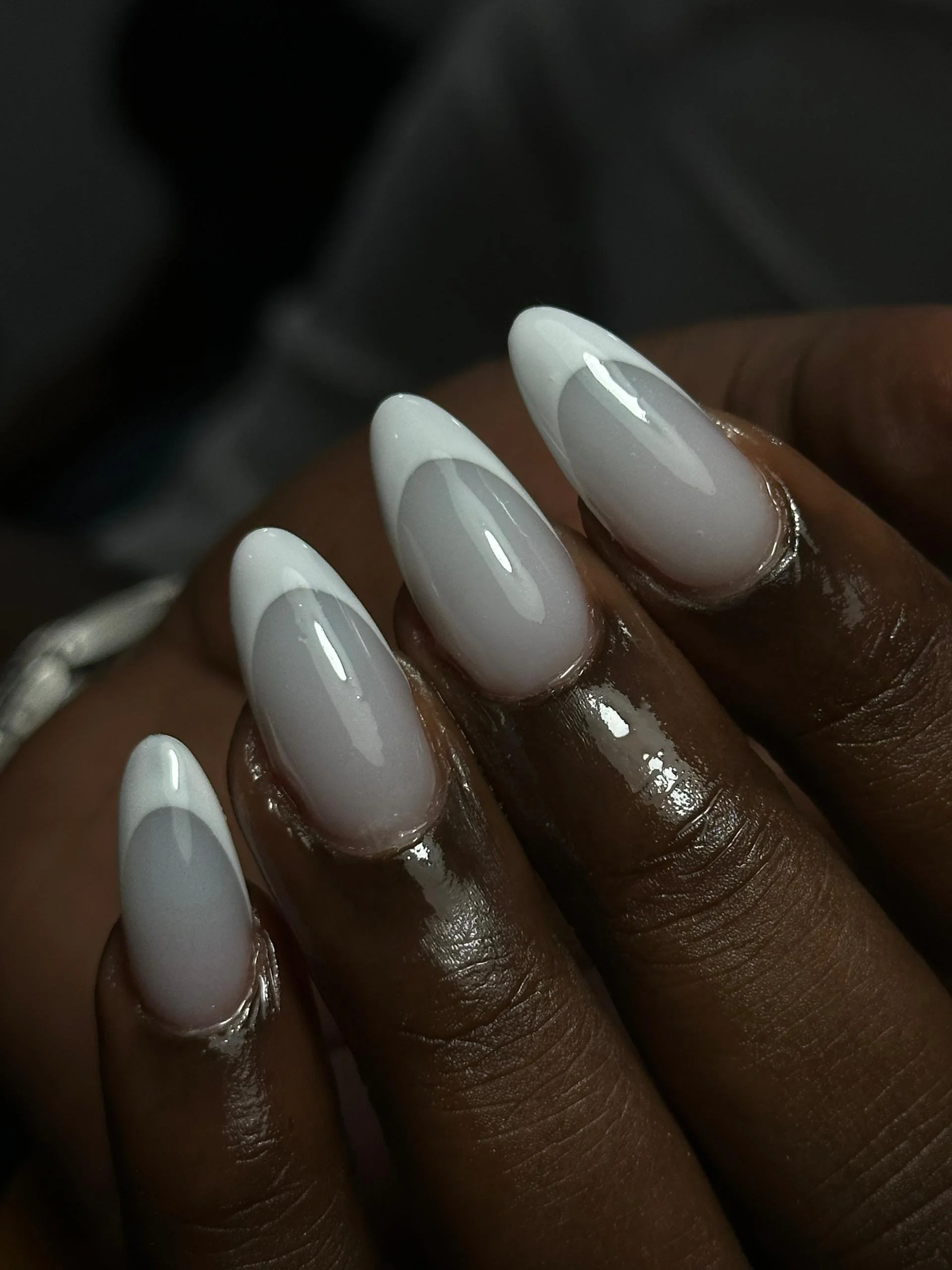 Close-up of manicured fingernails with white and gray ombre gel polish on darker skin.