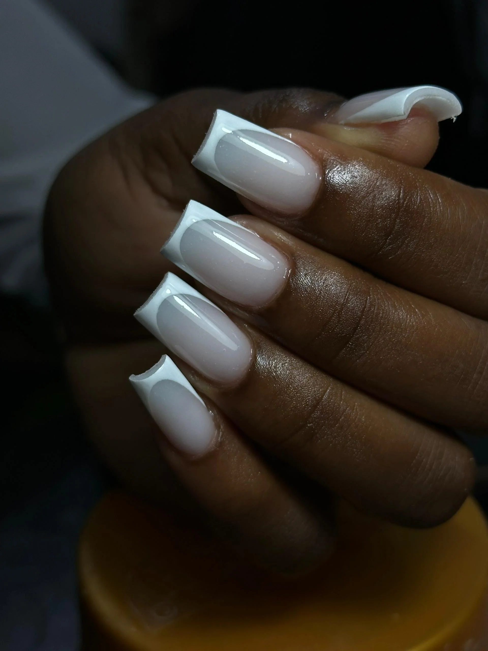 Close-up of a person's hand with manicured nails painted in a white color, showing the nails from different angles.