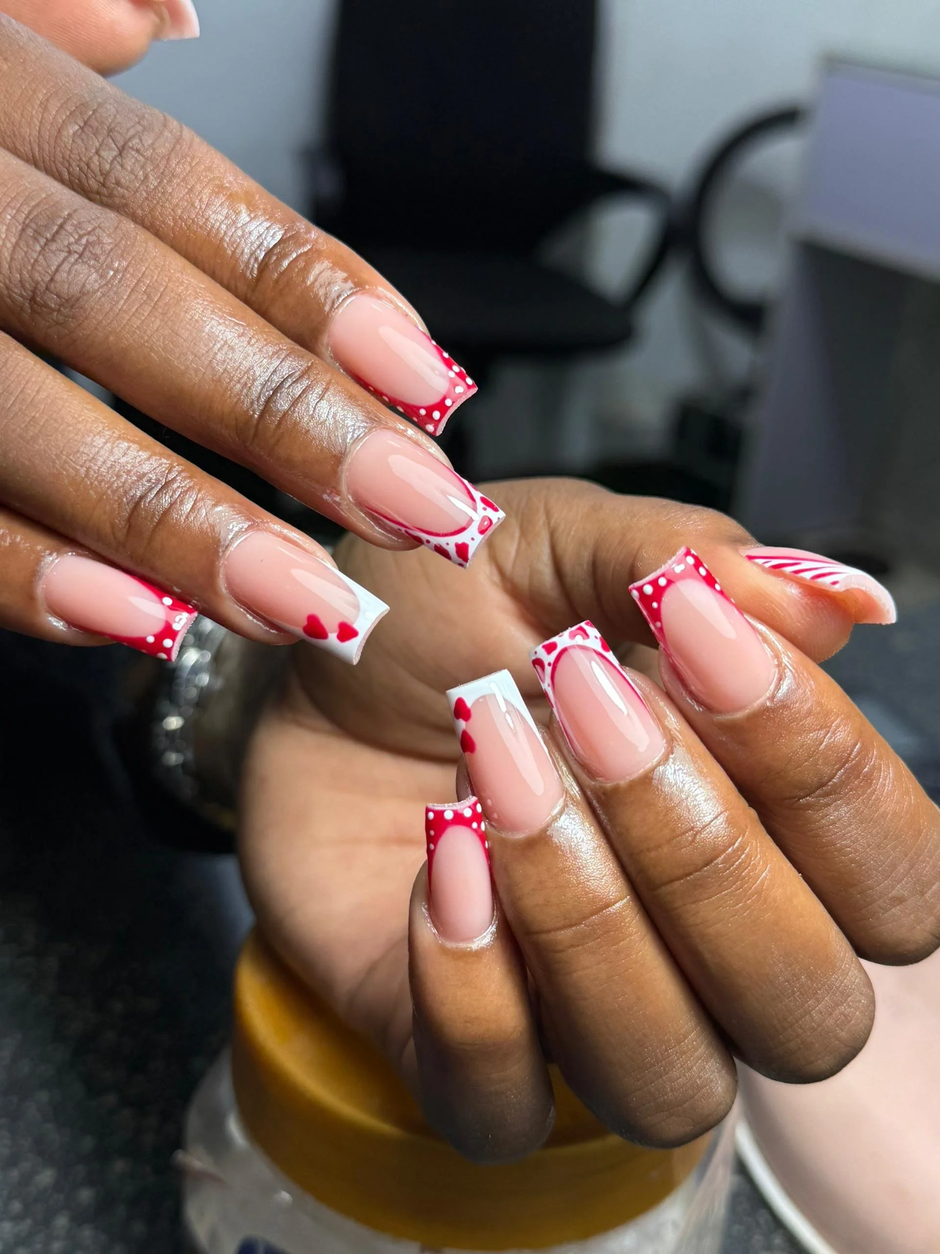 Close-up of hands with freshly manicured nails featuring red, white, and pink heart and dot designs.