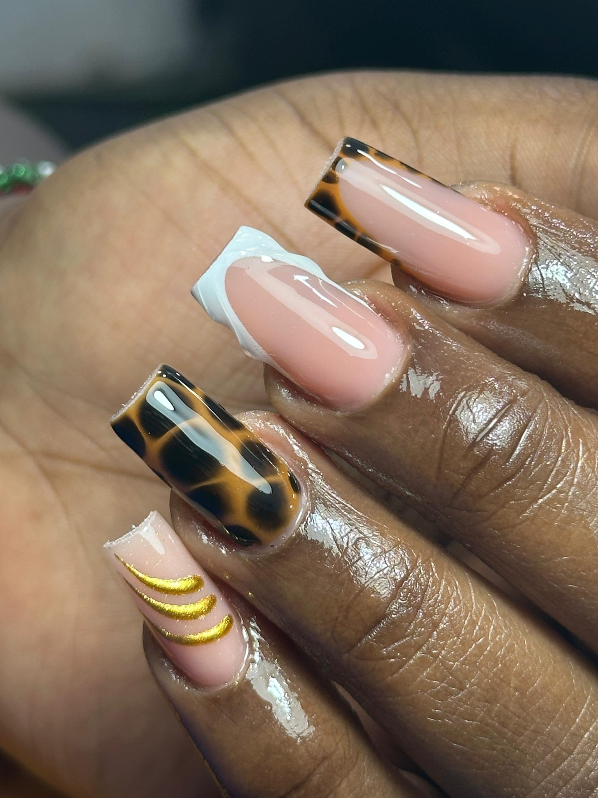 Close-up of a hand with manicured nails featuring a variety of designs, including tortoise shell patterns, gold accents, and a plain beige color.