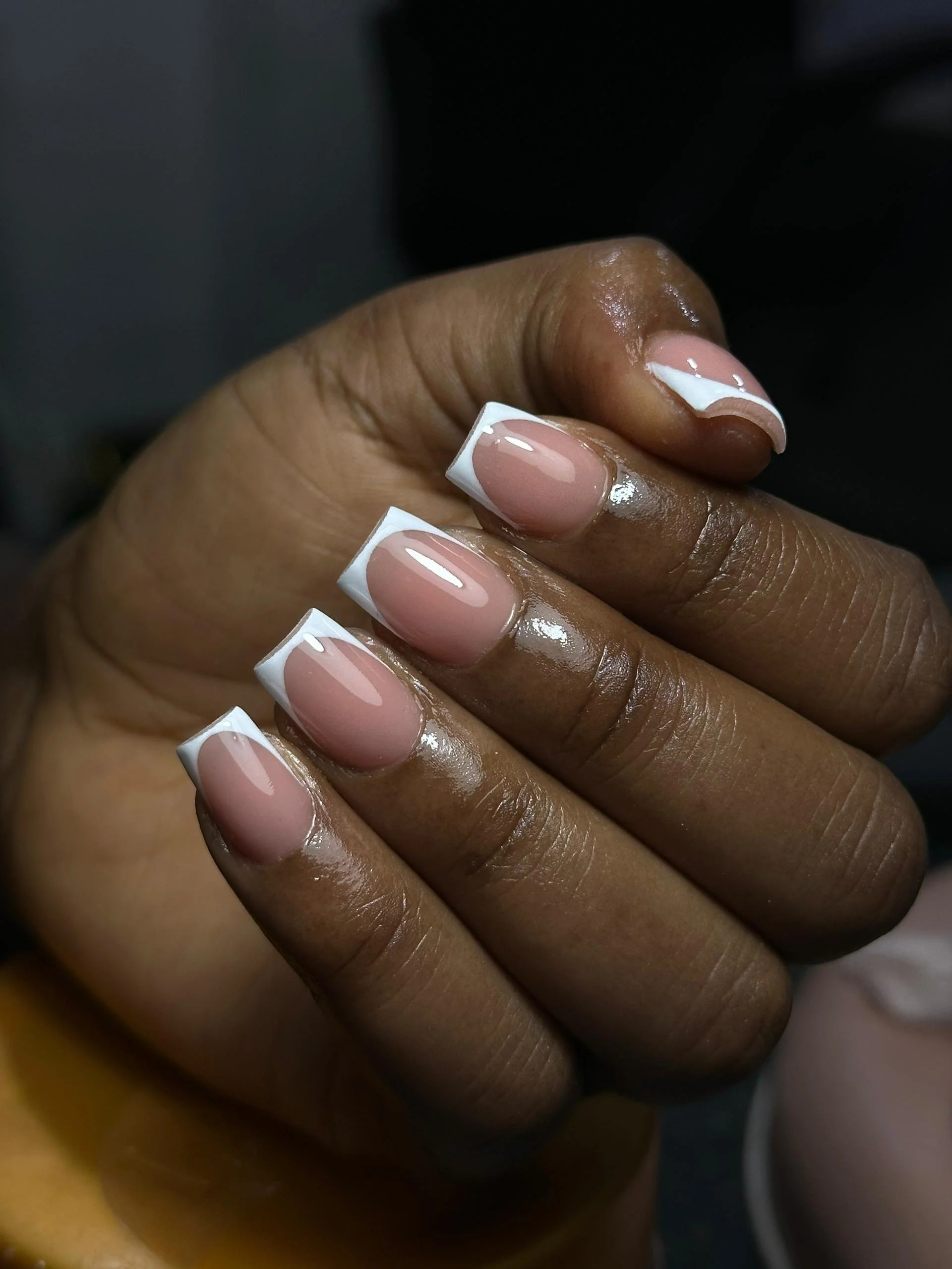 Close-up of a person's hand with freshly manicured nails featuring a classic French tip design, with white tips and a natural pink base.