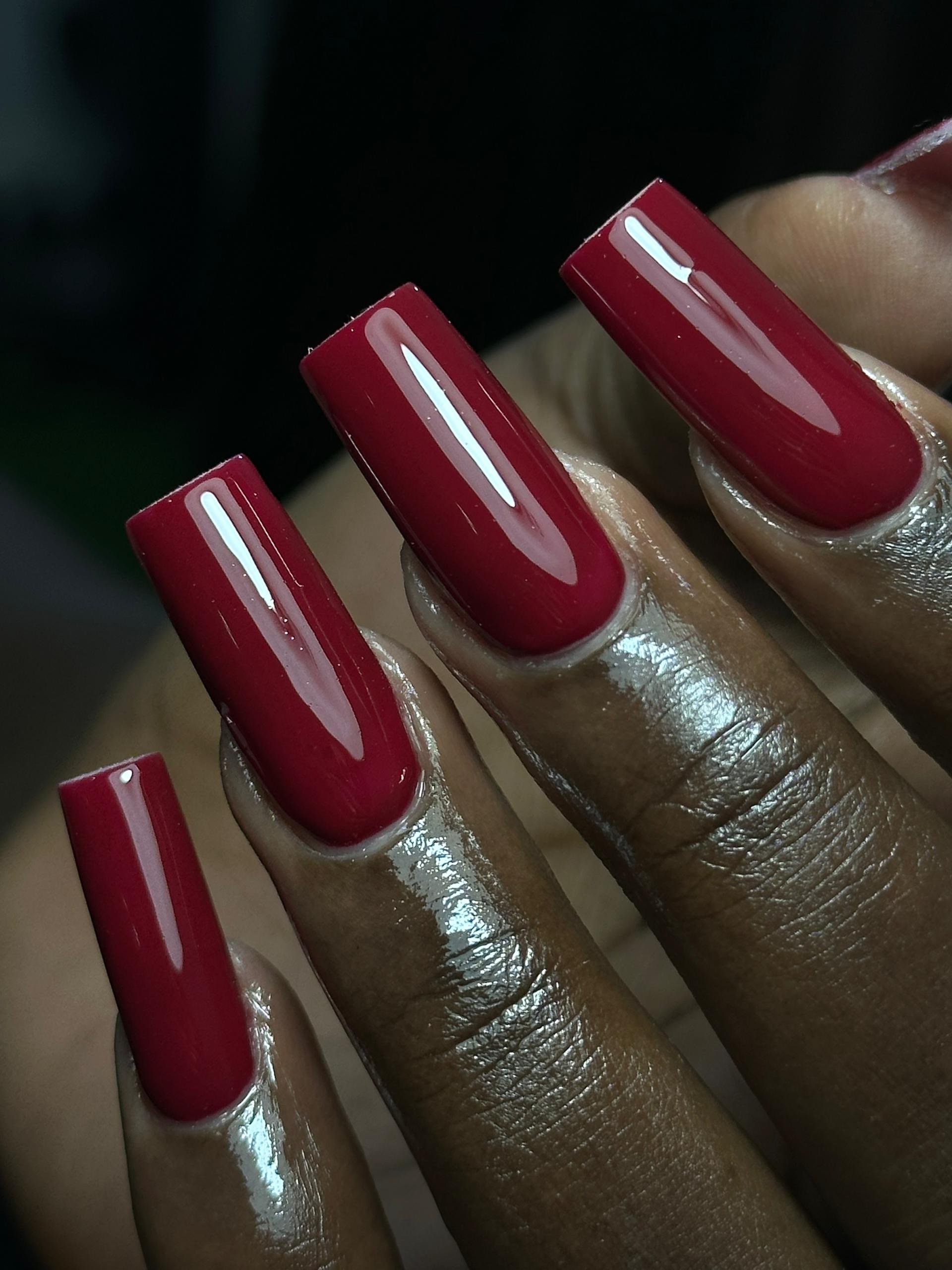 Close-up of four fingers with long, glossy, red-painted nails.