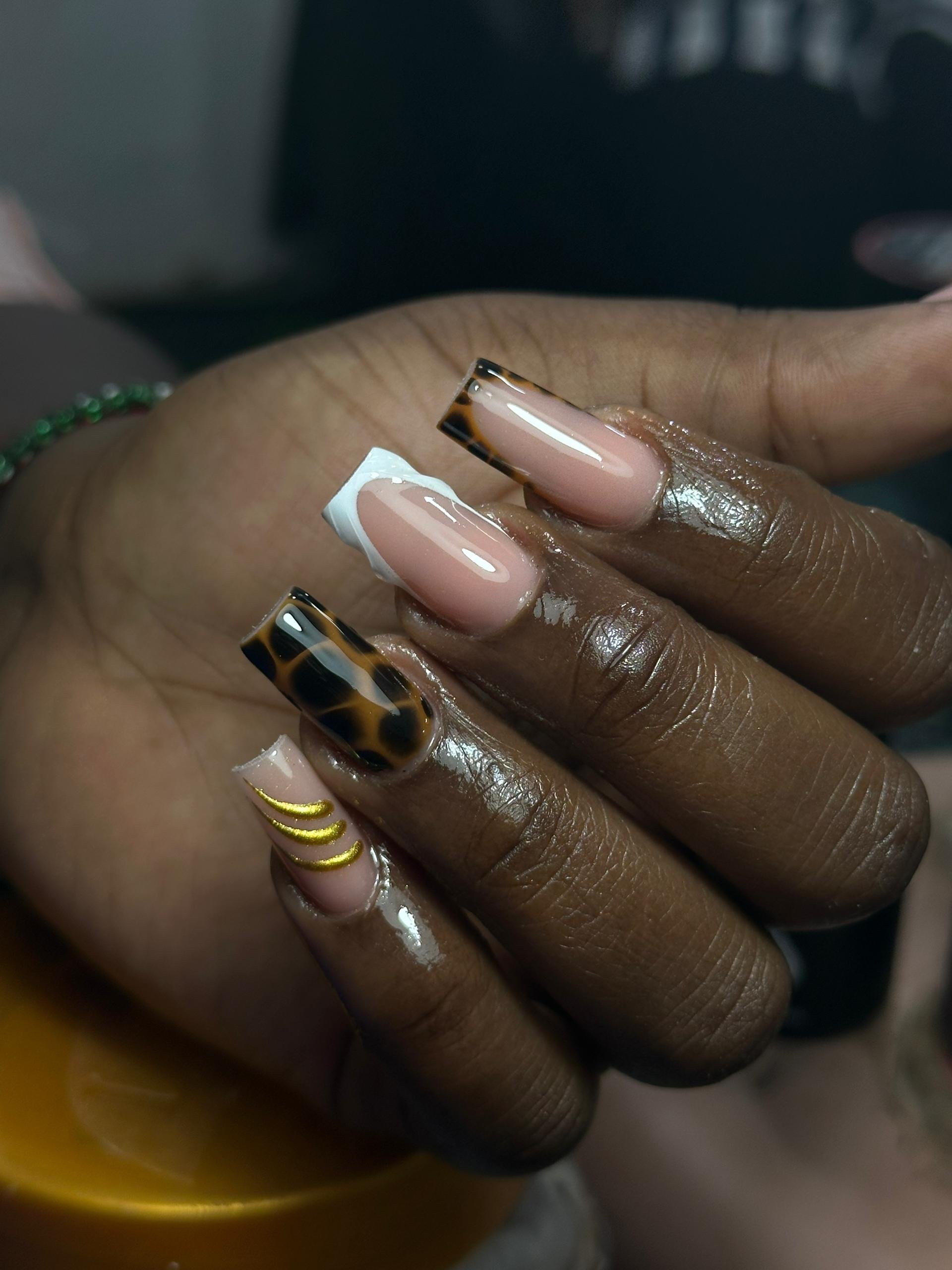 Close-up of a hand with manicured nails in a variety of designs, including tortoise shell, white with white tip, and gold accents.