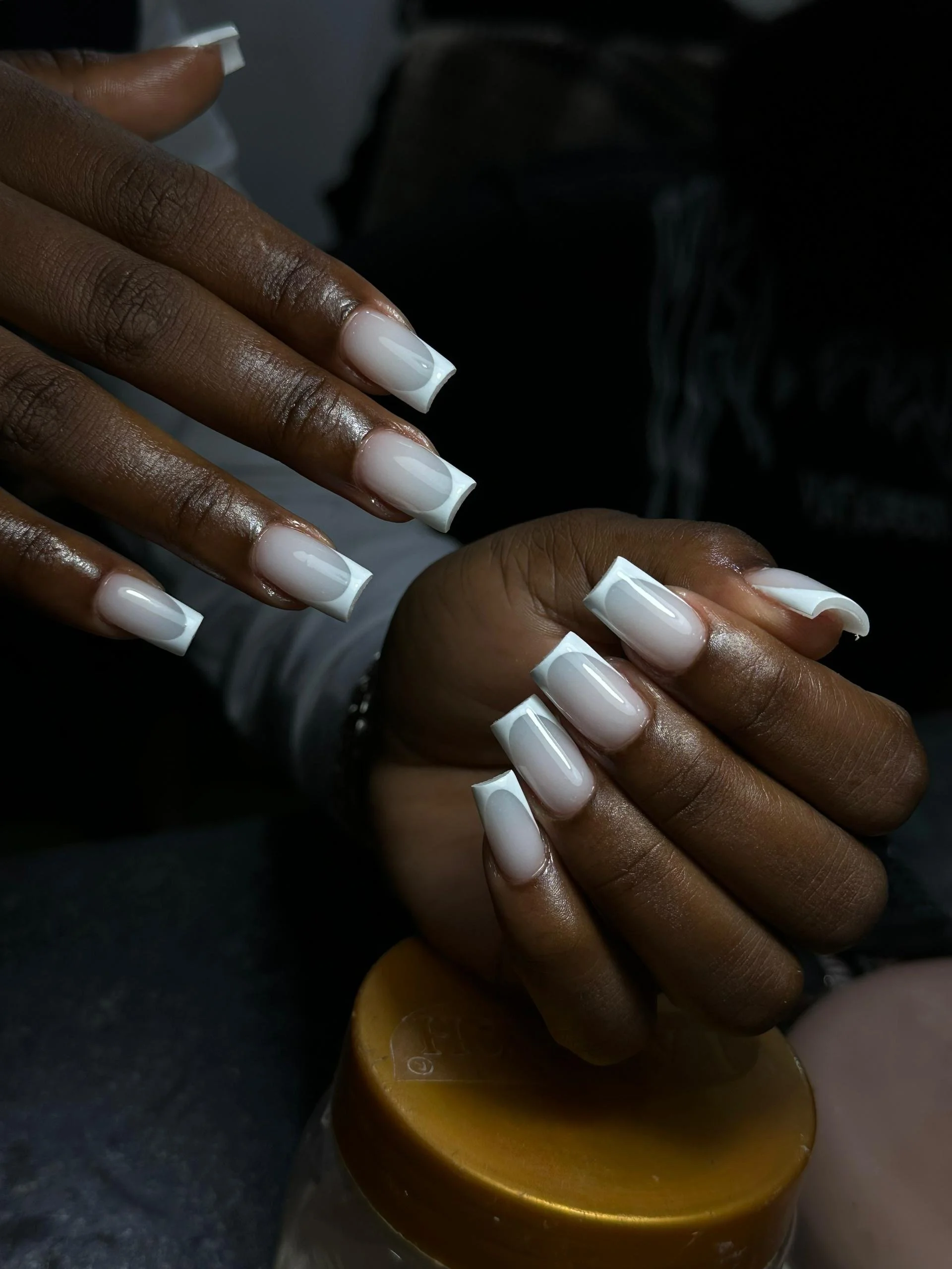 Hands with freshly manicured nails painted in a glossy pale pink color, with the left hand resting on a surface and the right hand held above.