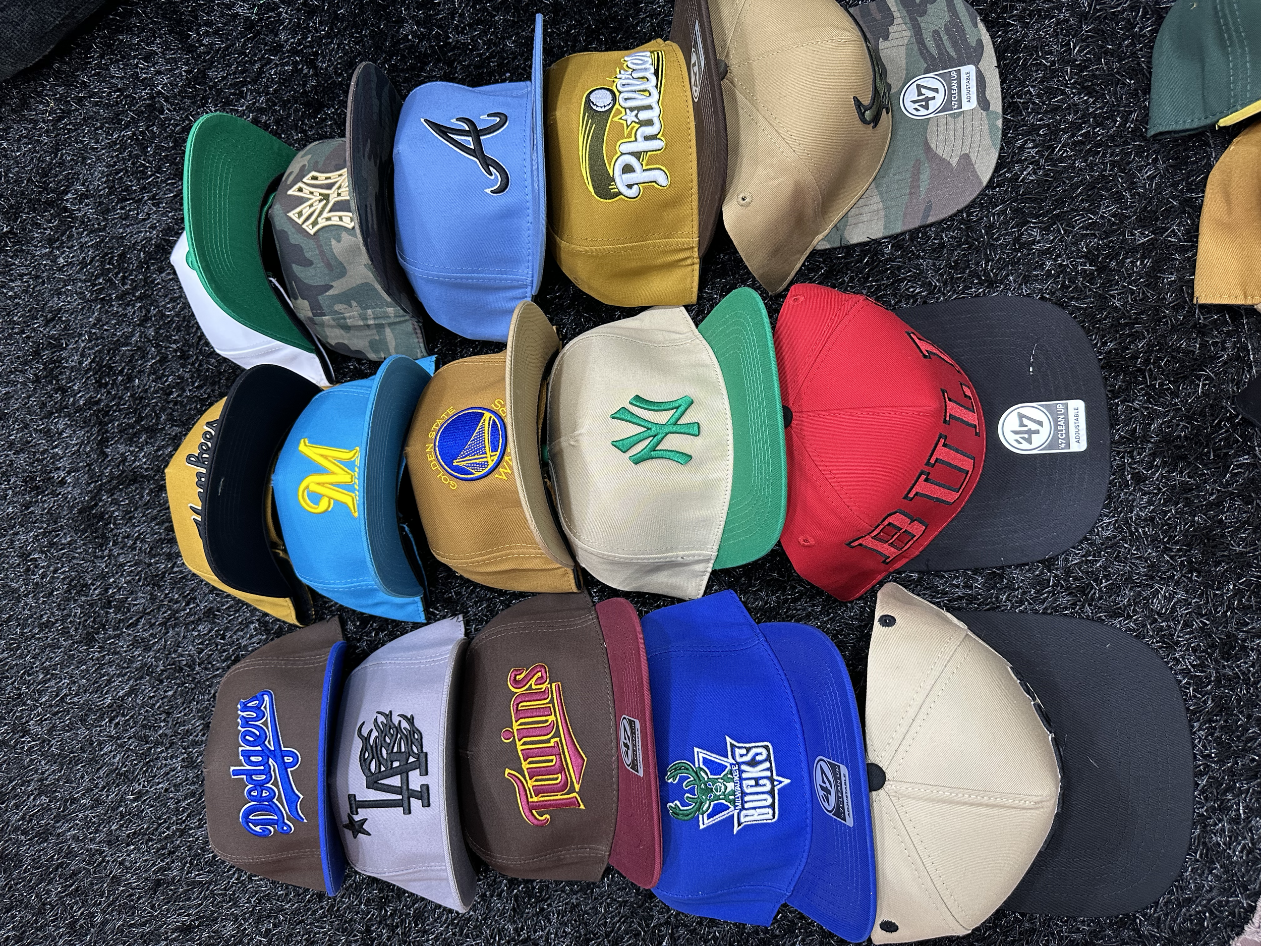 A collection of baseball caps, each representing different Major League Baseball teams, arranged on a dark textured surface.