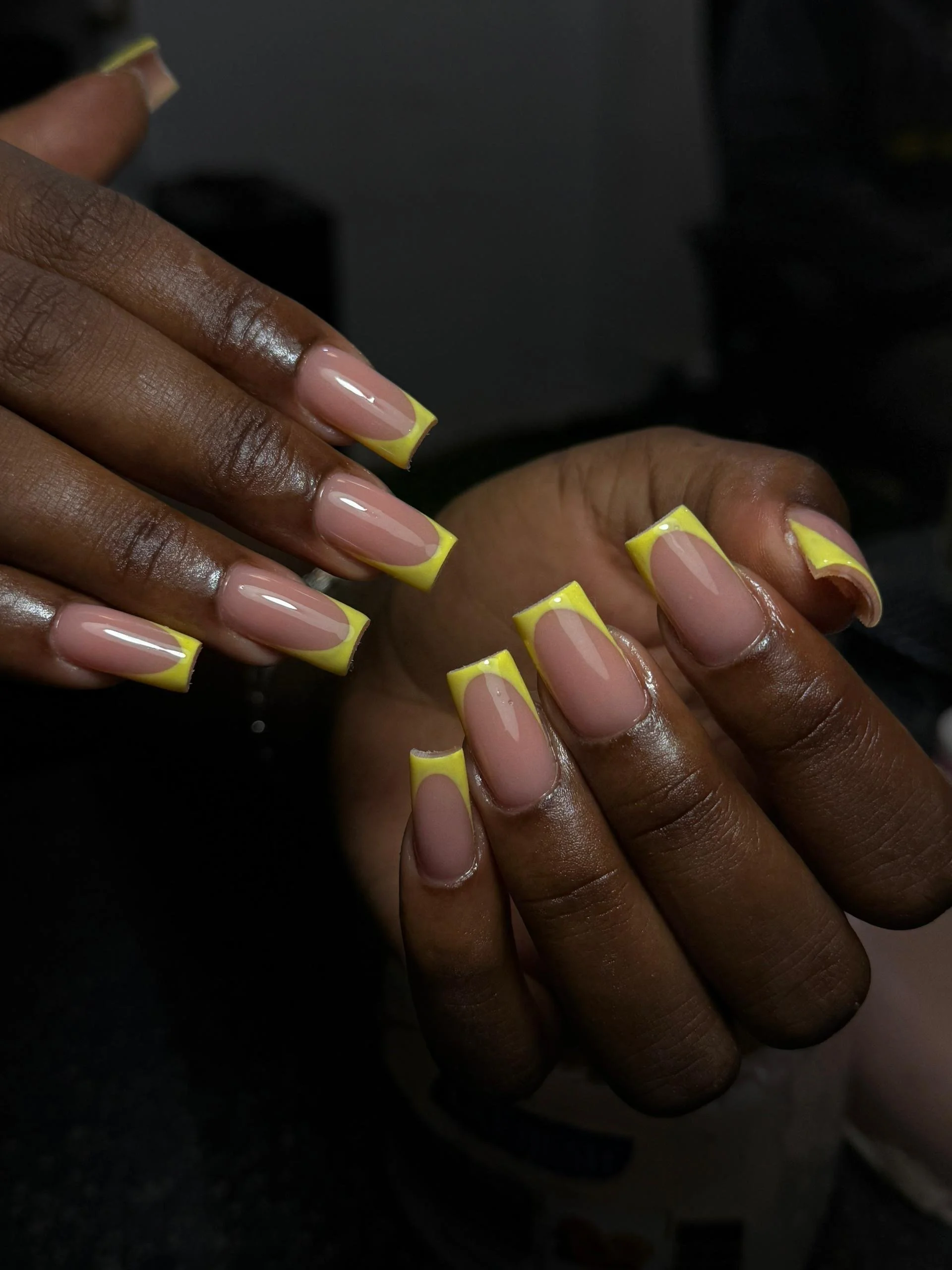 Close-up of two hands with manicured nails, featuring pink polish with yellow French tips.