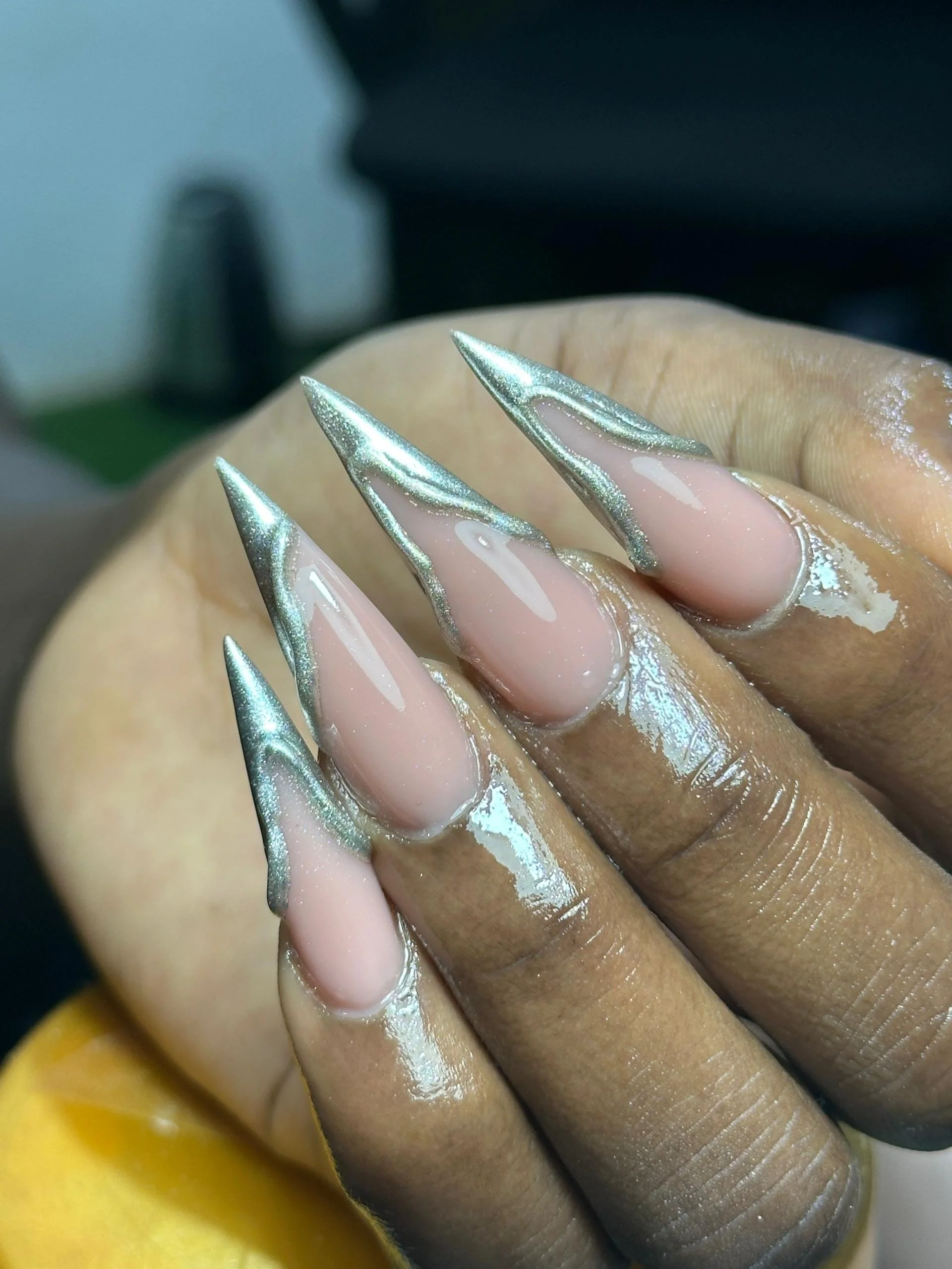 Close-up of a hand with long, pointed nails painted with shiny, metallic silver tips and a nude base, possibly during a manicure process.