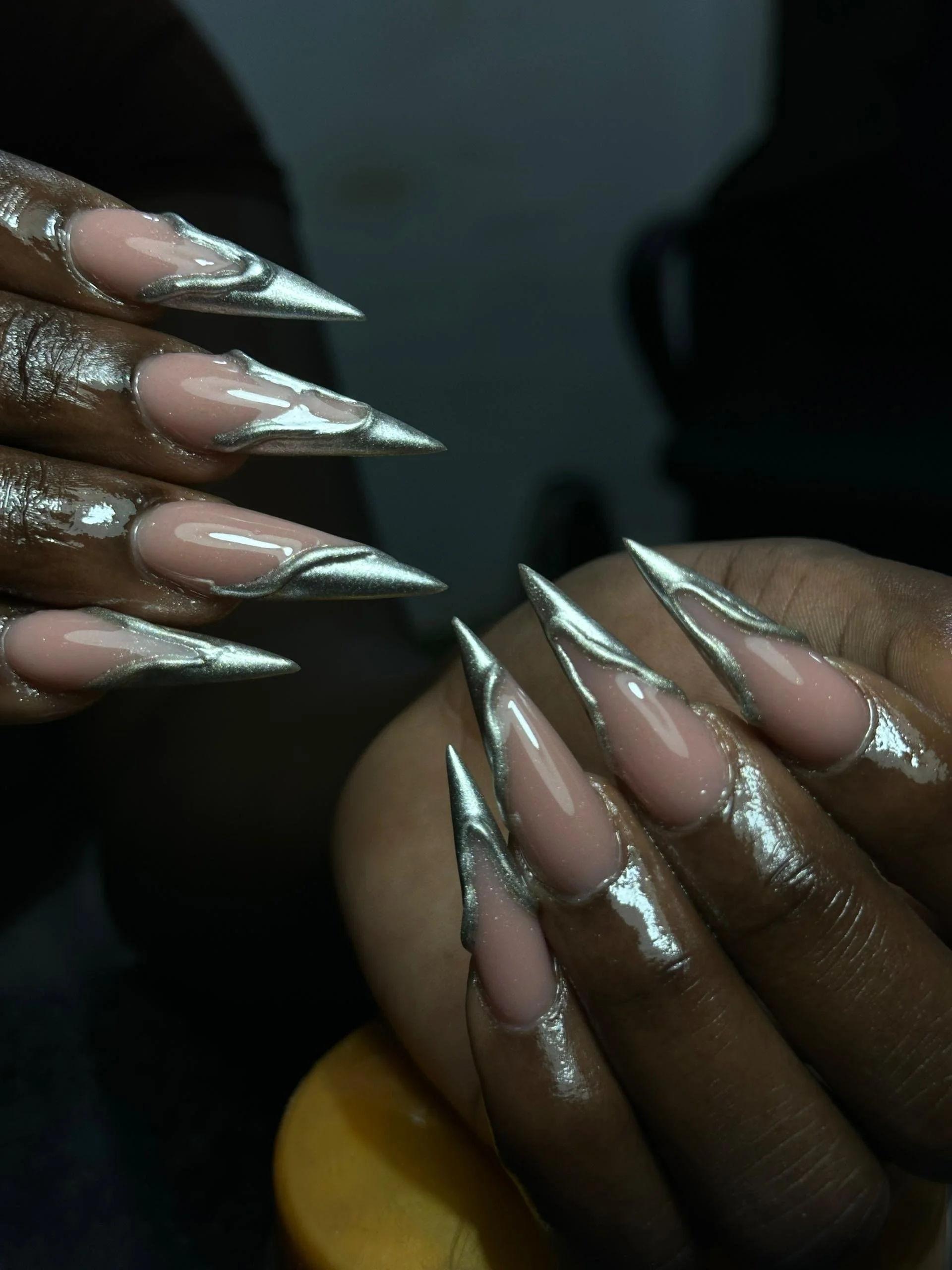 Close-up of a person's hands with long, pointed nails painted with a shiny silver gradient design.