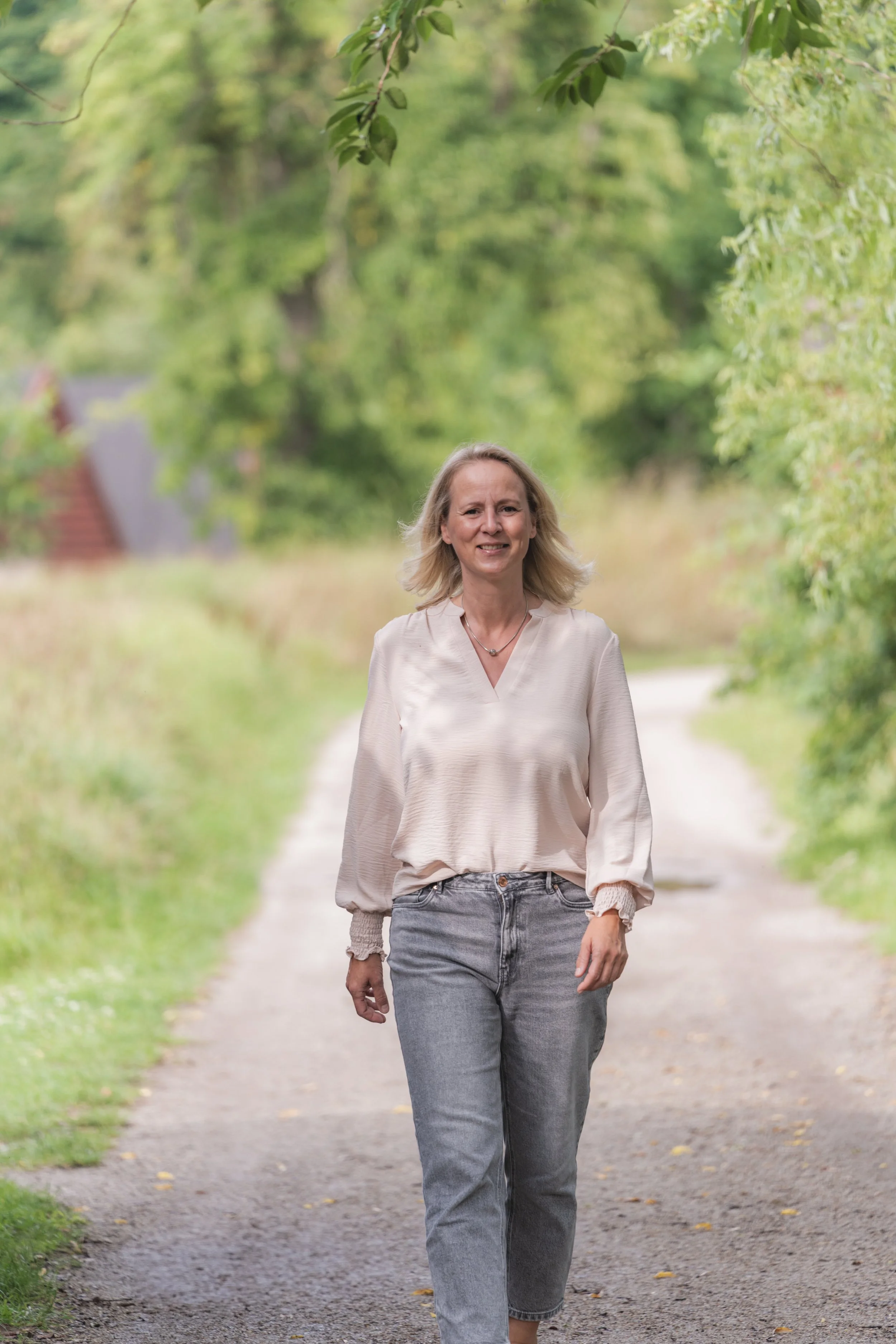 Eine Frau geht auf einem Weg in einer grünen, baumbeschatteten Naturumgebung.