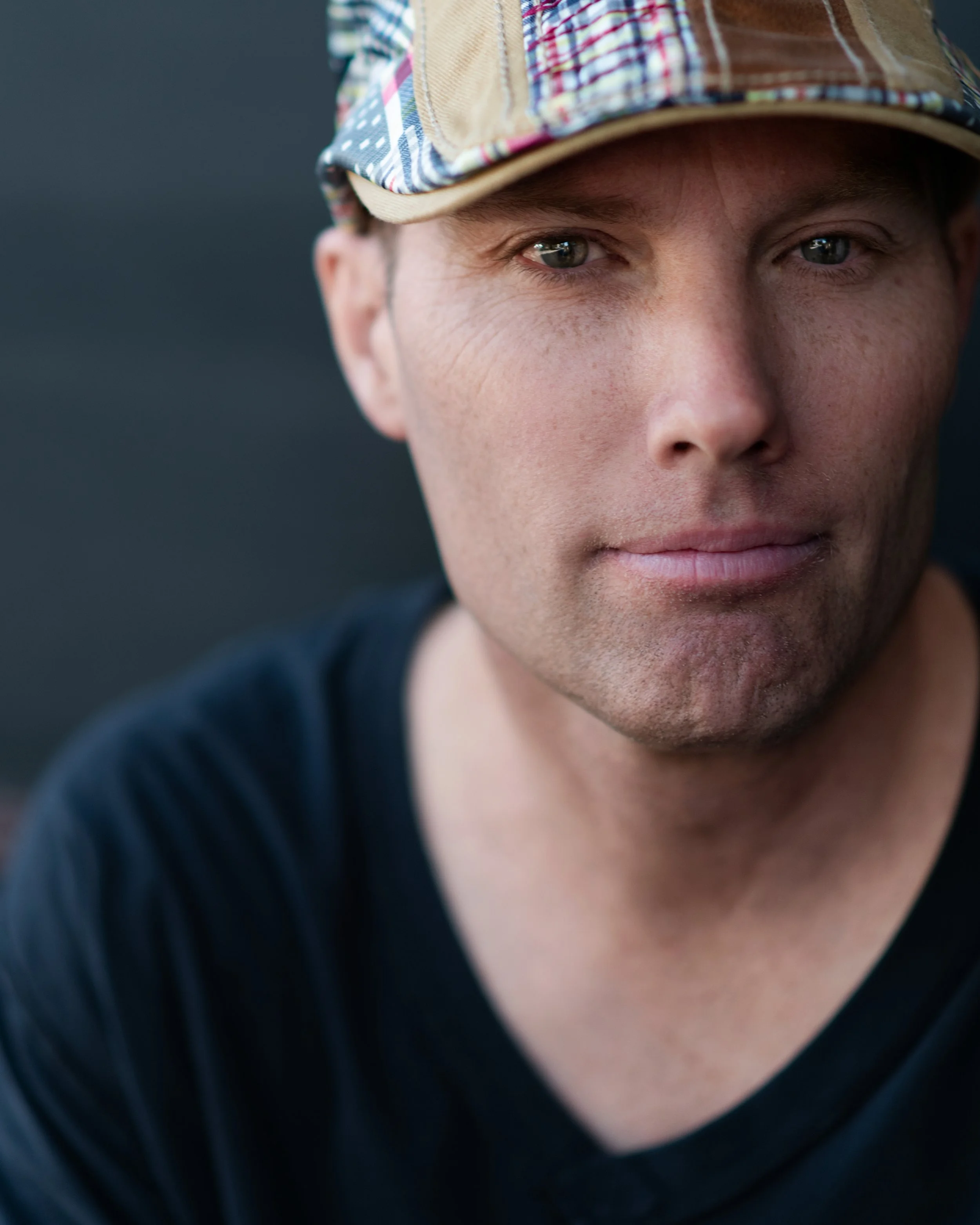 Close-up of a young man's face, wearing a plaid cap, with visible freckles and blue eyes, and a dark shirt.