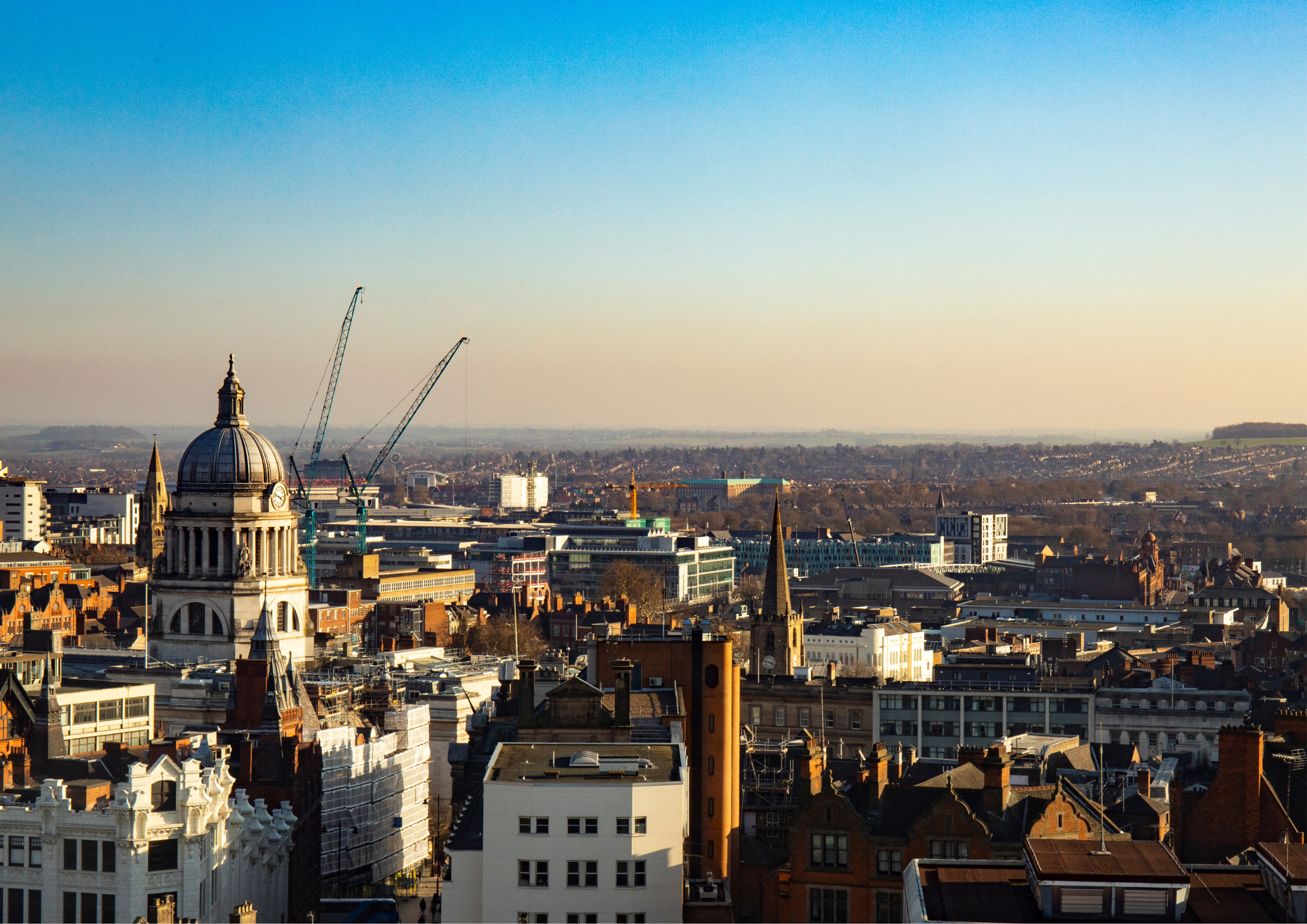 City skyline with historic buildings and modern construction cranes against a clear blue sky.
