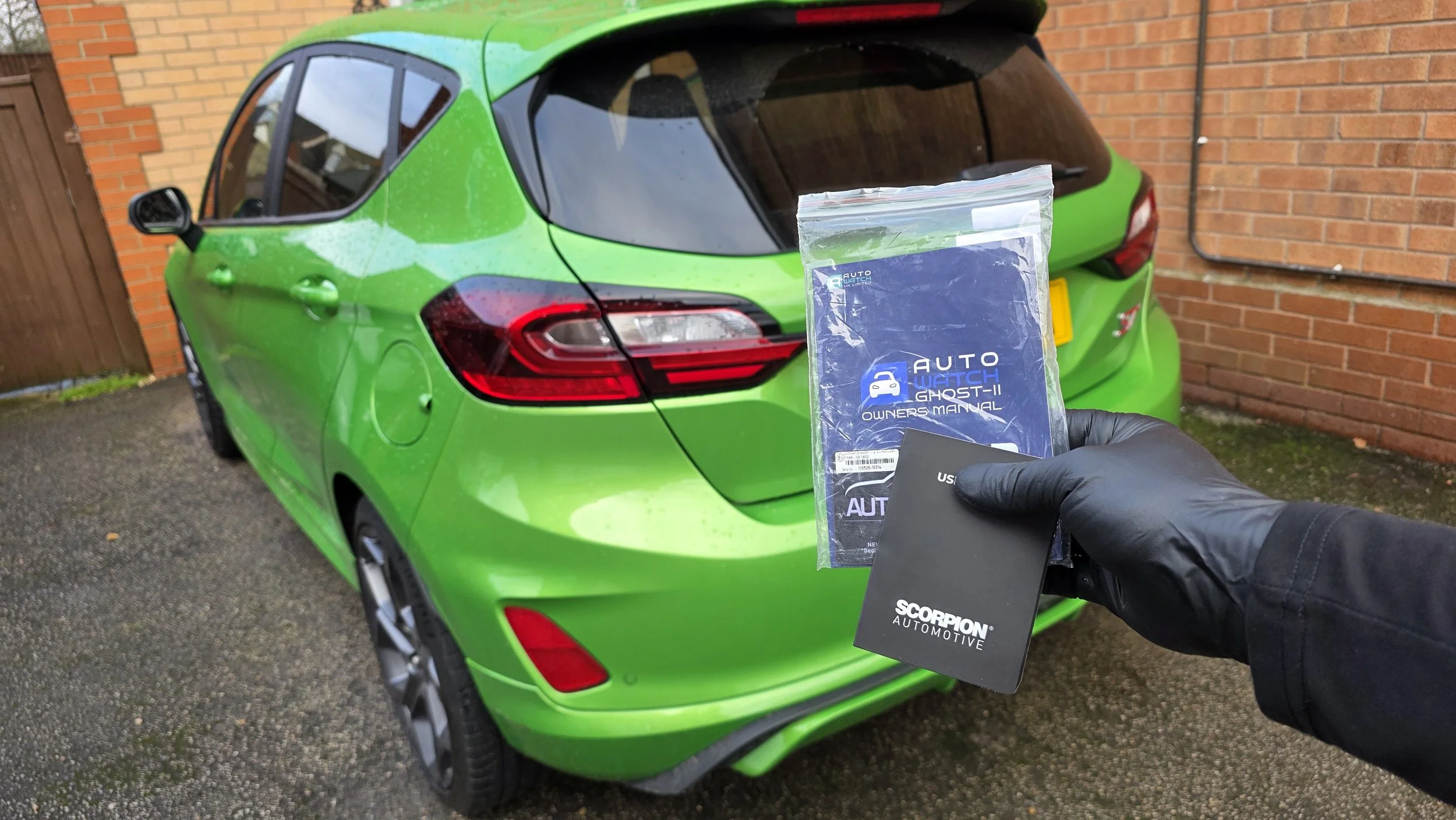 ScorpionTrack vehicle security system ready for installation beside a green Ford Fiesta.