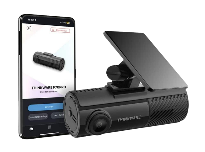 A black Thinkware F70 Pro dash camera connected to a smartphone app displaying its live view and settings.