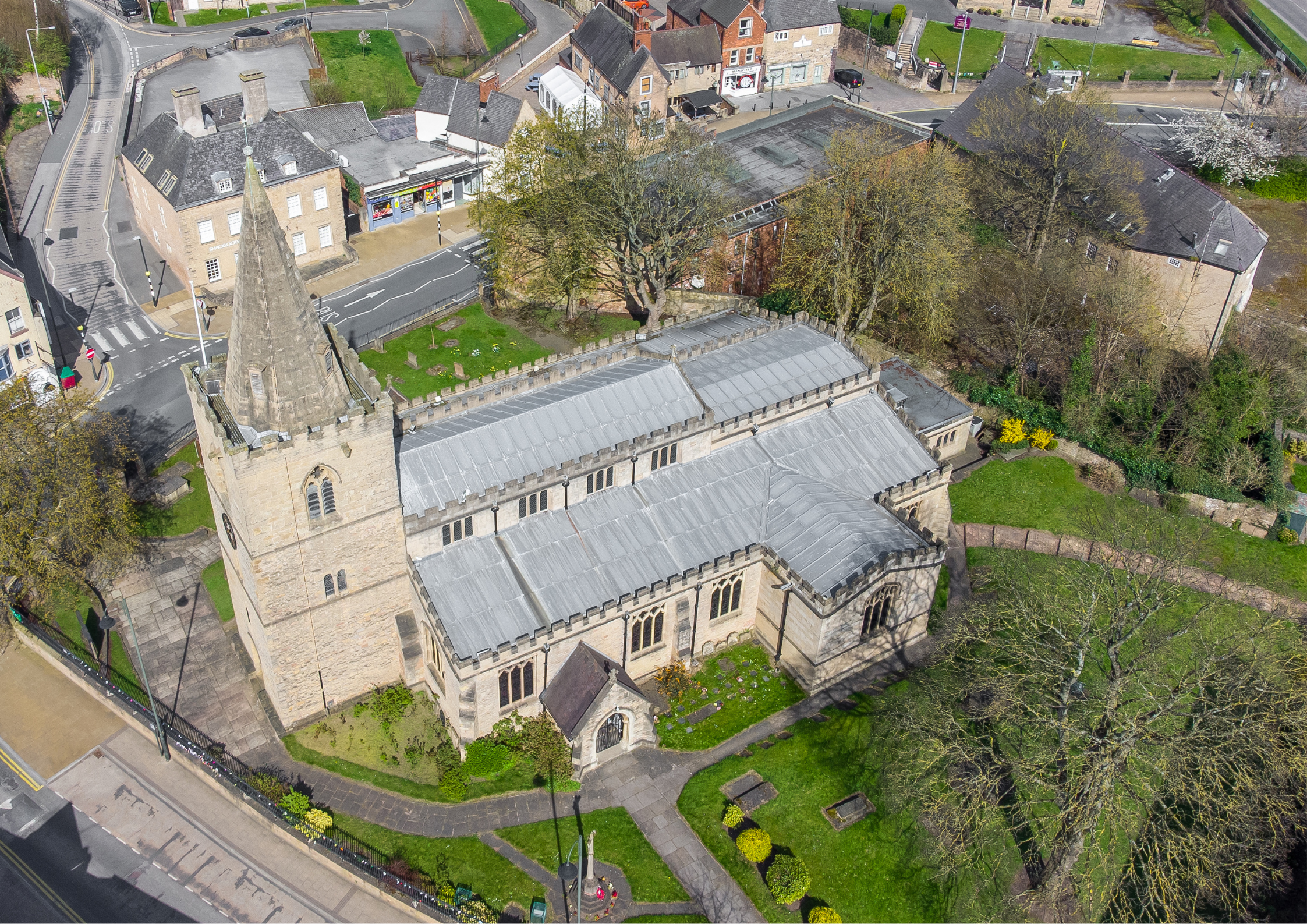 Aerial view of a church with a stone steeple, surrounded by streets, trees, and residential buildings in a small town.