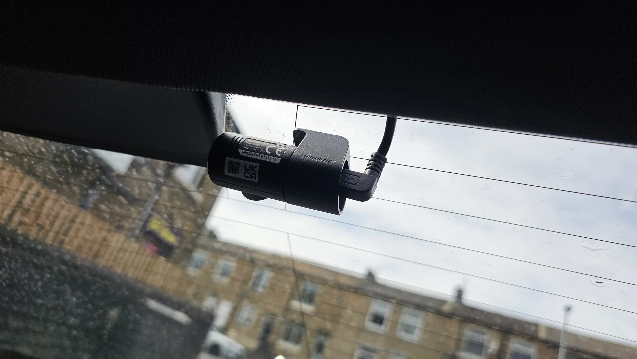 Device attached to the rear windshield of a vehicle, with buildings and power lines visible through the glass.