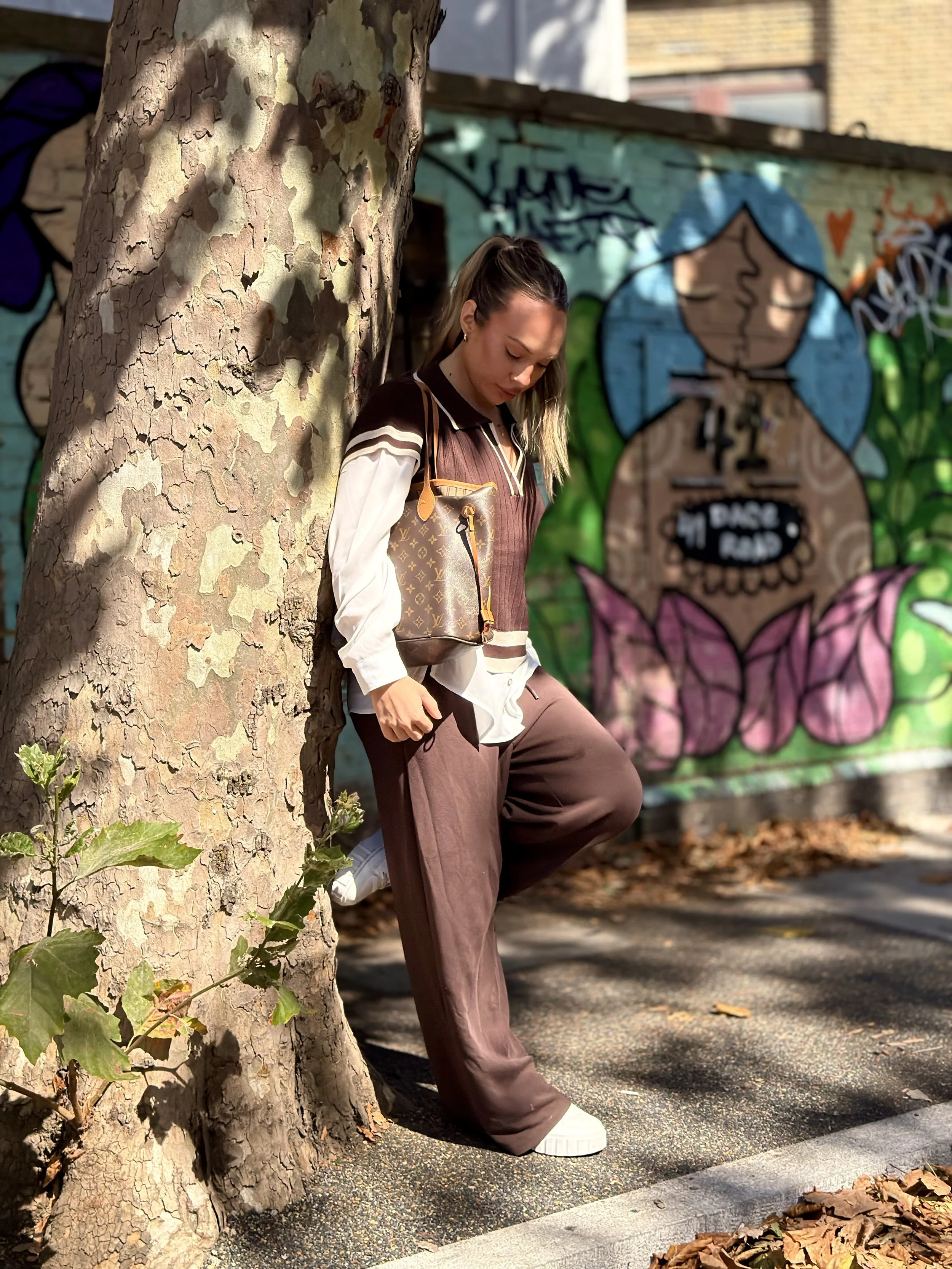 A woman leaning against a tree on a sidewalk with graffiti art on the wall behind her.