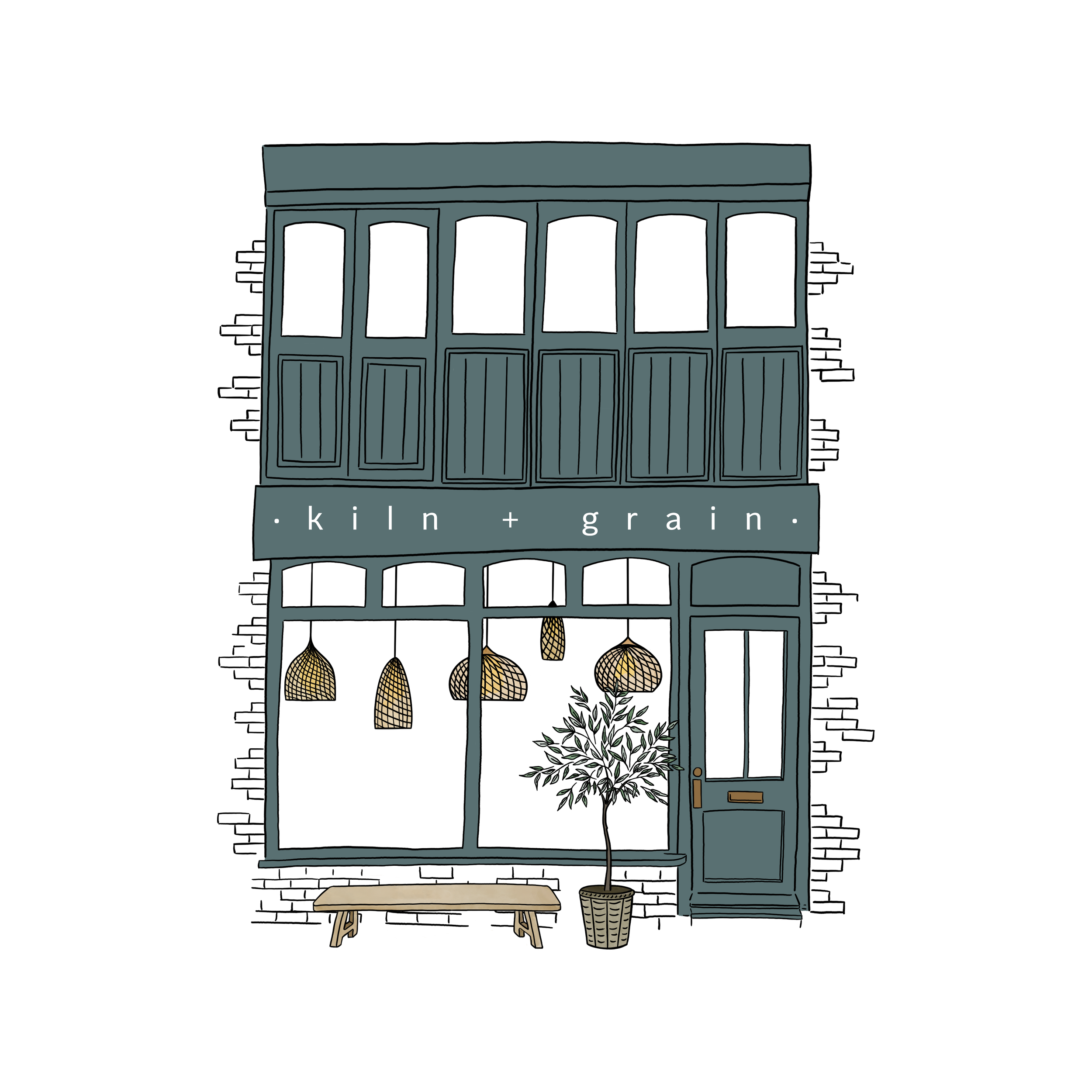 A two-story storefront with a dark teal exterior, large window display on the ground floor showing hanging woven pendant lights, a small tree in a pot, and a wooden bench outside, with a sign reading 'kiln + grain' above the window.