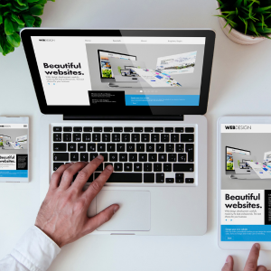 Laptop and smartphone displaying web design projects on a white desk with a potted plant in the background.