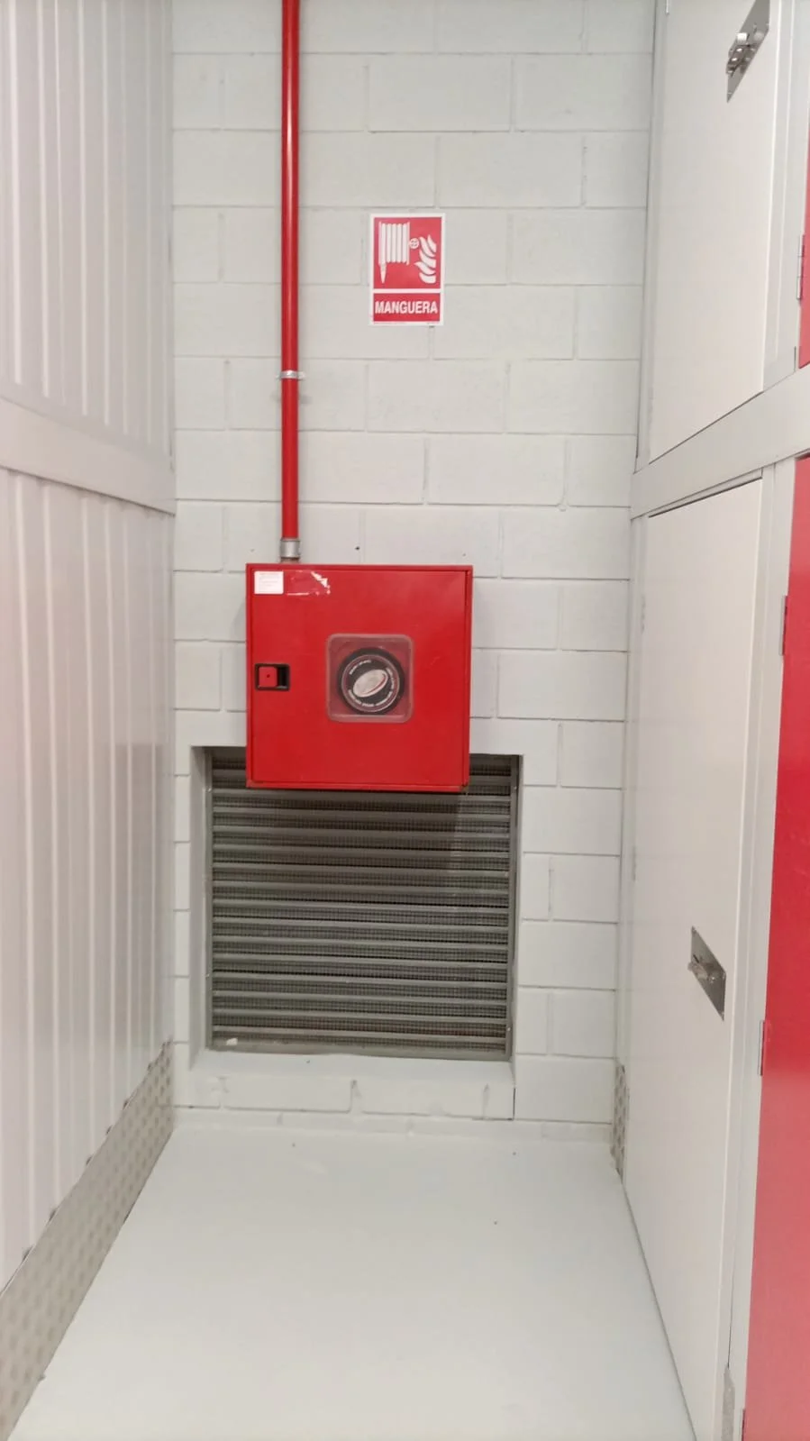 Sistema de rociador contra incendios con manguera y señal de advertencia en pared de cemento.
