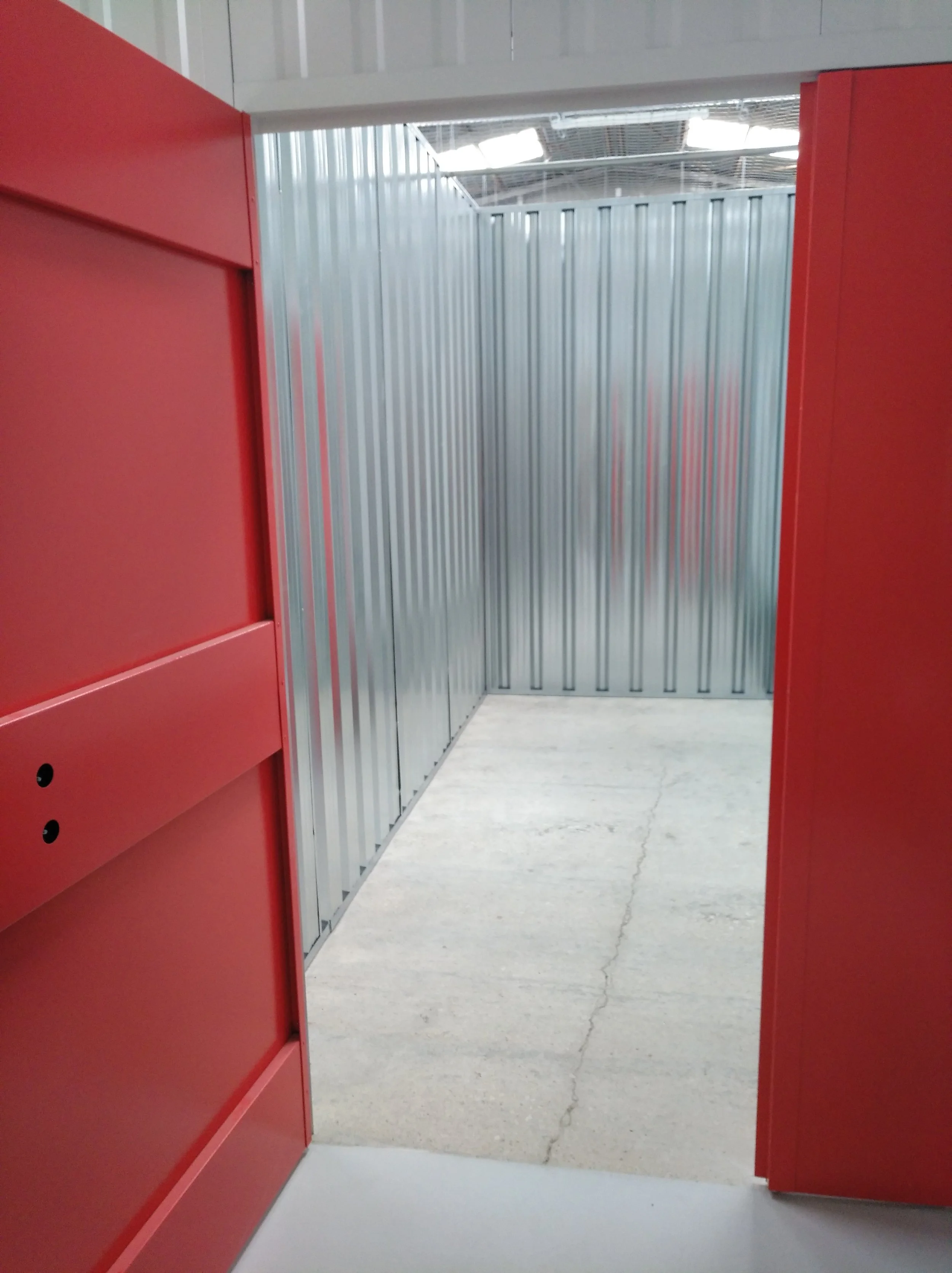 Entrada a un espacio con paredes metálicas plateadas y puertas rojas a los lados, piso de concreto con grietas.