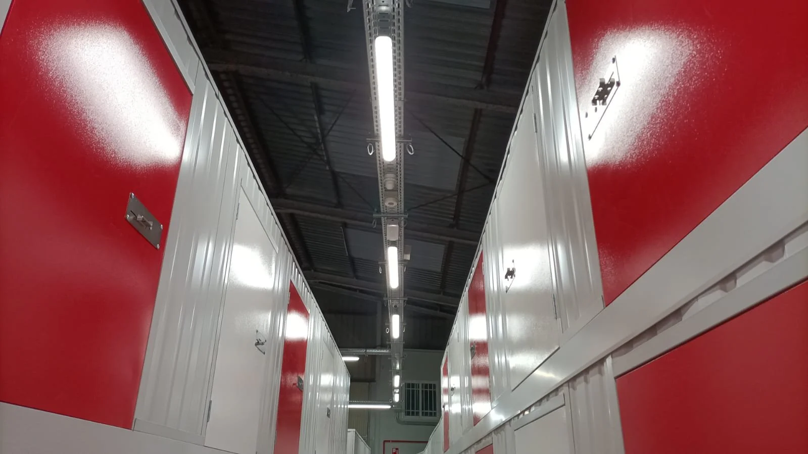 Pasillos con gabinetes blancos y rojos en un espacio de almacenamiento moderno, con iluminación fluorescente en el techo.