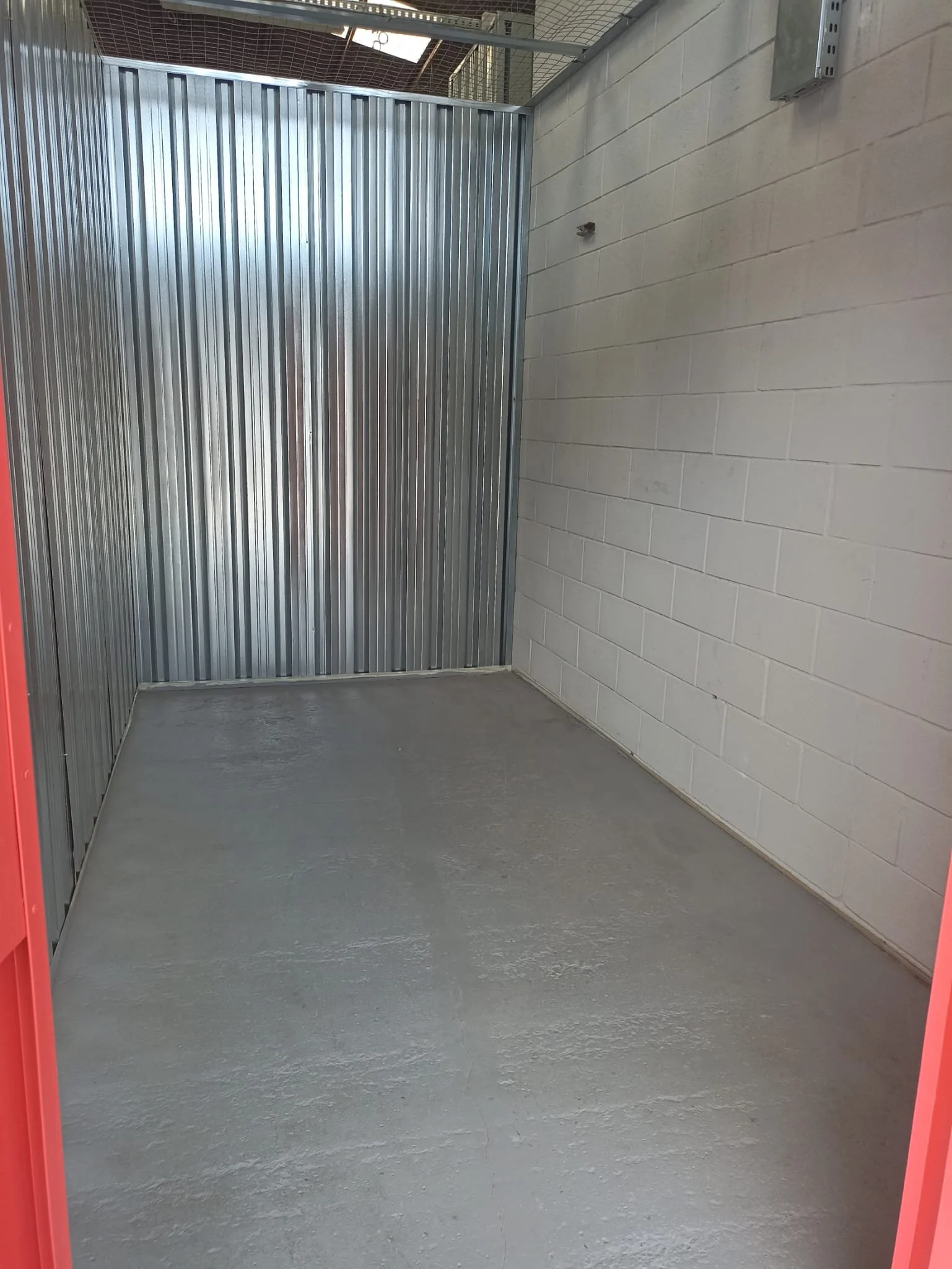 Espacio vacío con paredes de ladrillo, piso de concreto y una estructura metálica, posiblemente un contenedor o habitación en construcción o reparación.