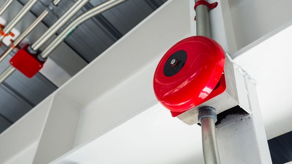 Caja roja con un círculo negro en el centro, fijada a una estructura metálica, probablemente una alarma o dispositivo de seguridad en un entorno industrial o de mantenimiento.
