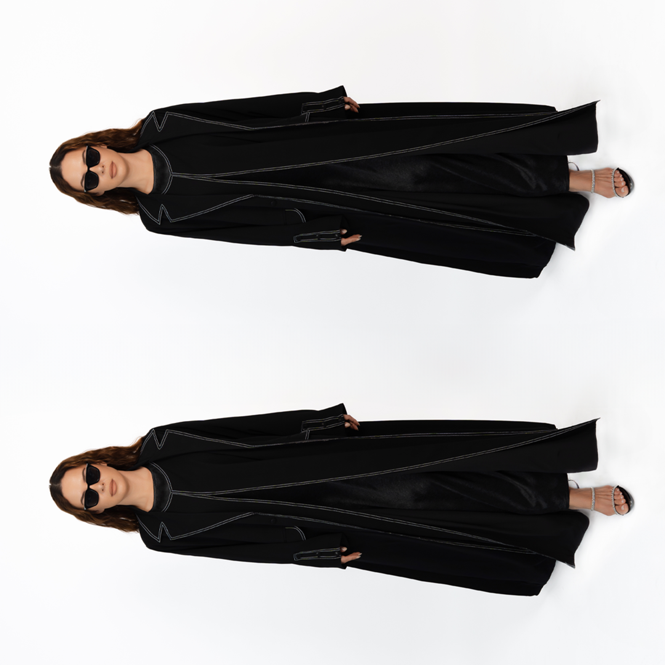 Woman standing in front of a white background, wearing a black coat, black sunglasses, and black heels, with her hair styled in loose waves.