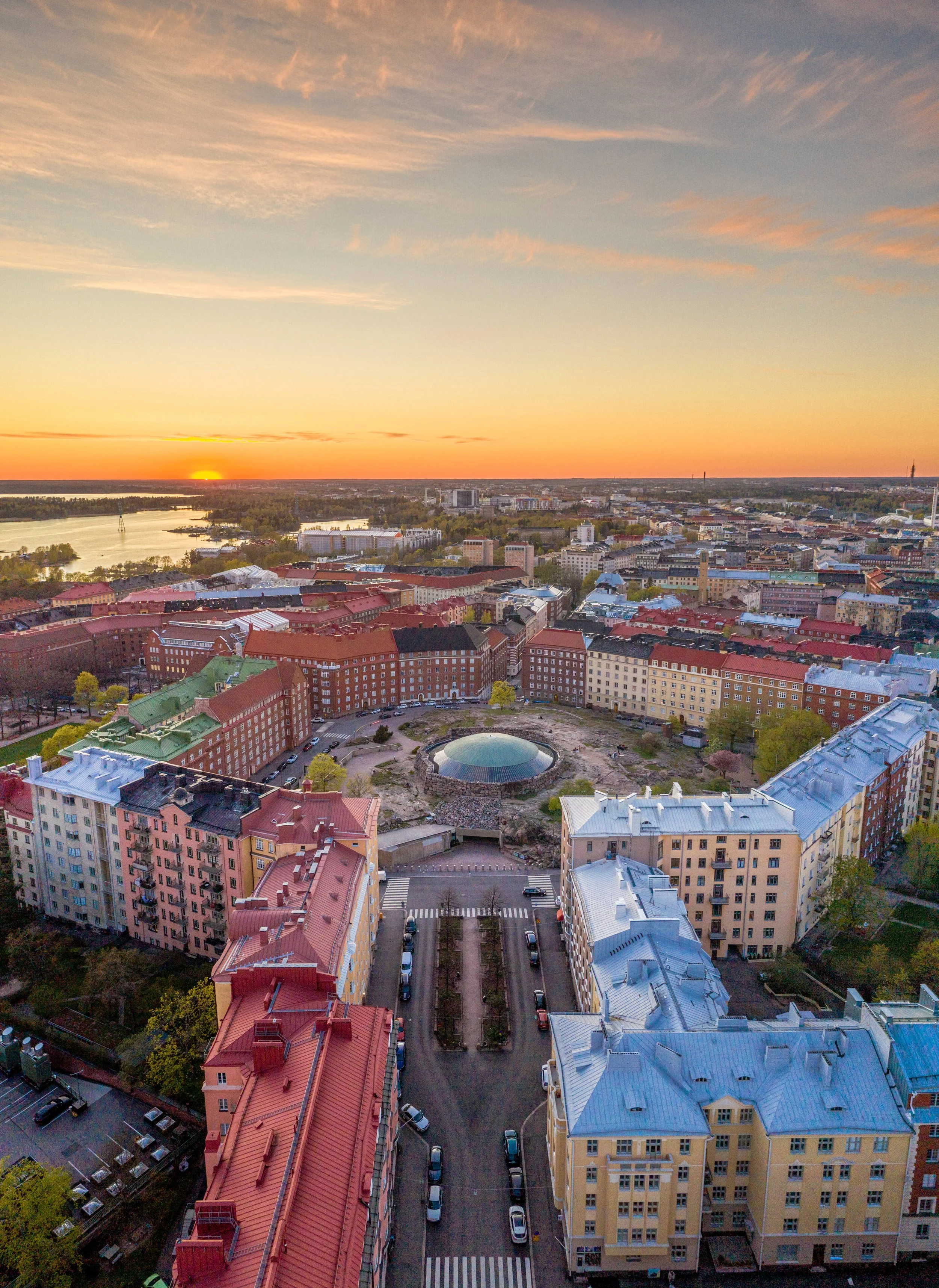 Aerial view of Töölö, Helsinki at sunset showing colorful buildings, a park with a water body, and a skyline in the distance.