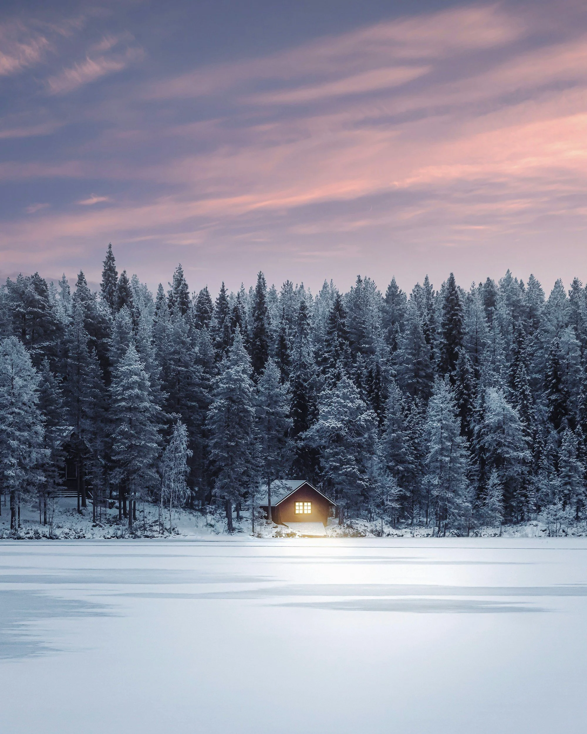 Warmly lit cabin surrounded by a snow-covered forest in Finnish Lapland