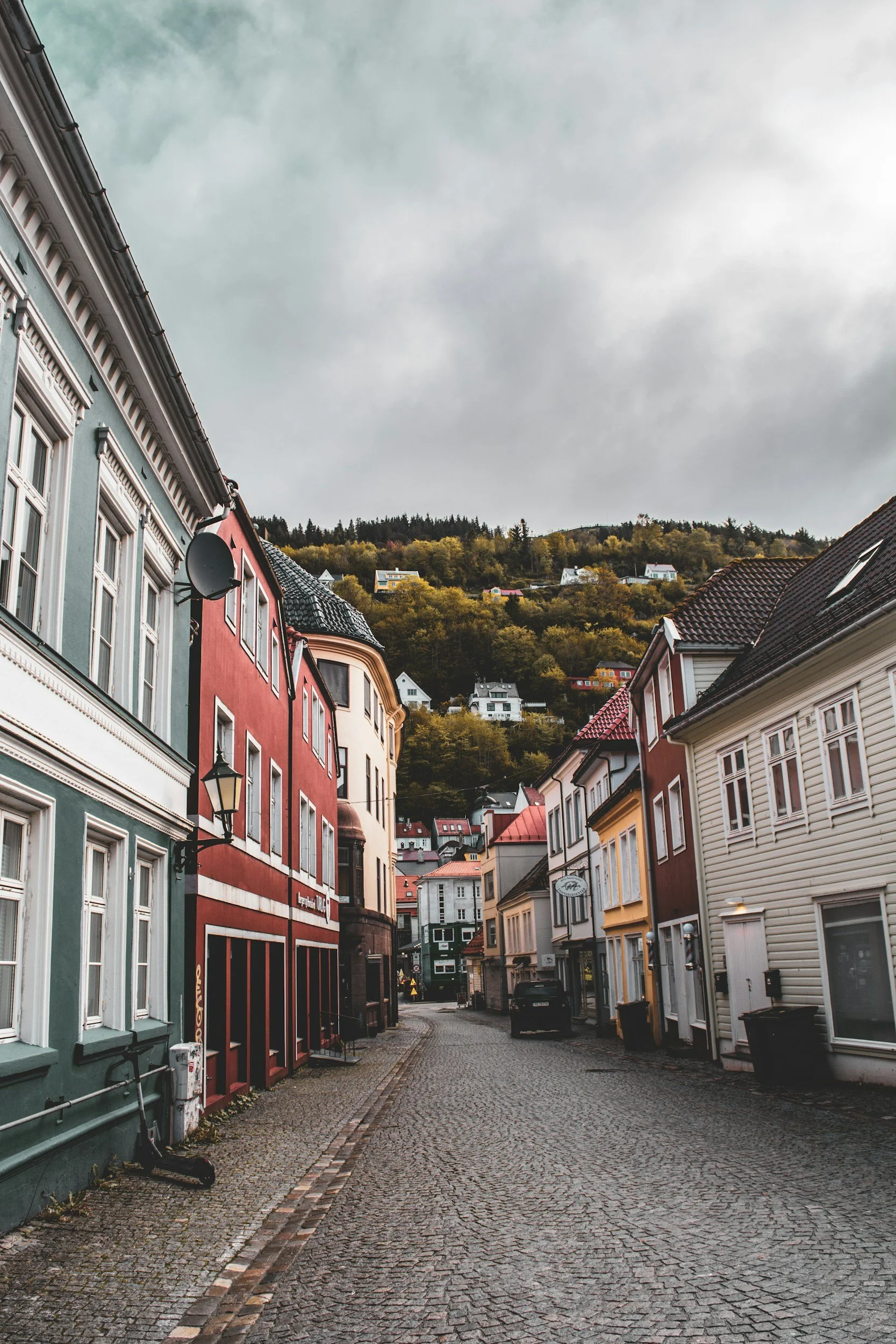 Colourful wooden houses lining a quiet cobbled street beneath the hills of Bergen, Norway.