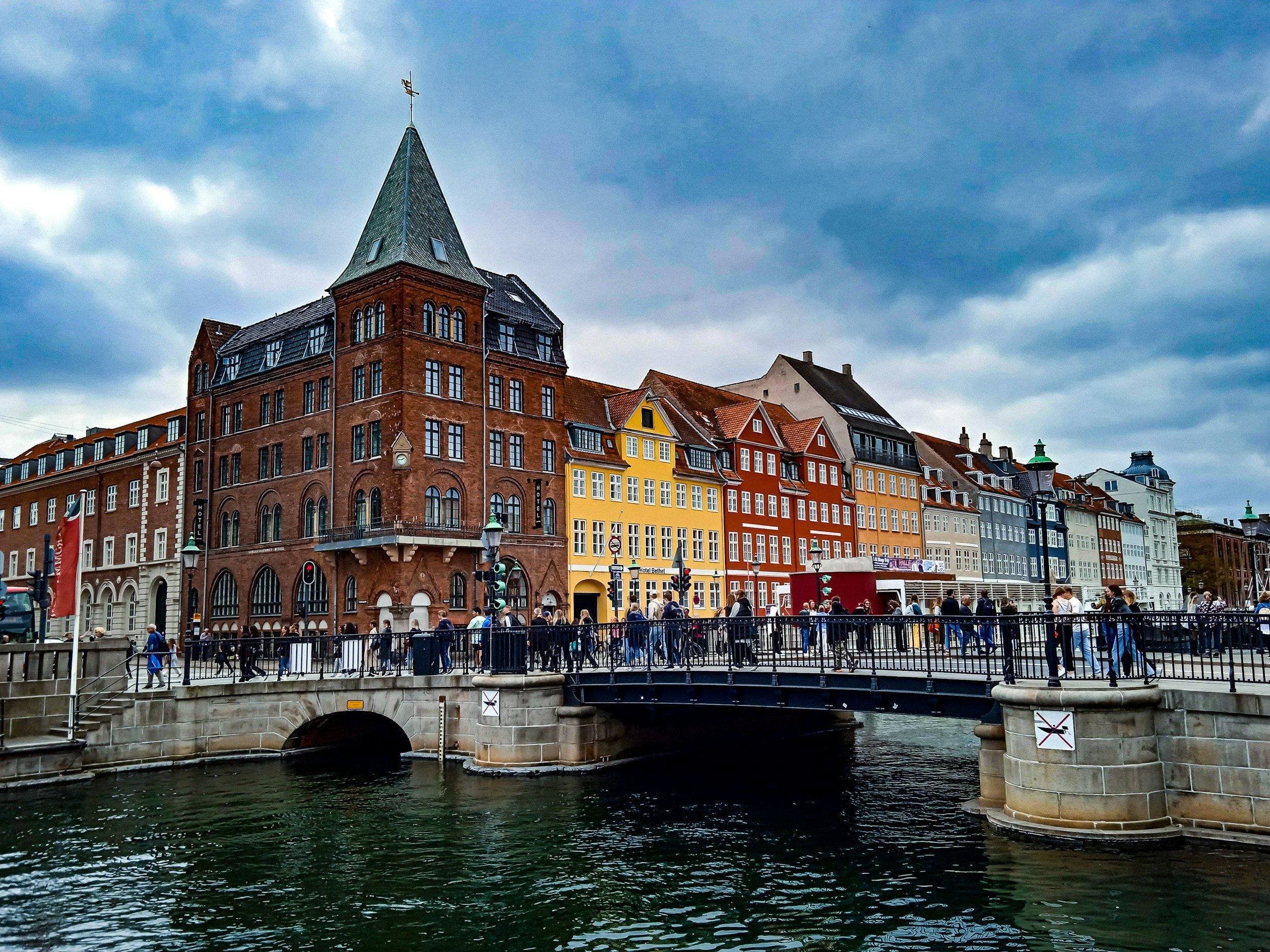 Colourful historic buildings and pedestrians beside a canal bridge in central Copenhagen, Denmark.