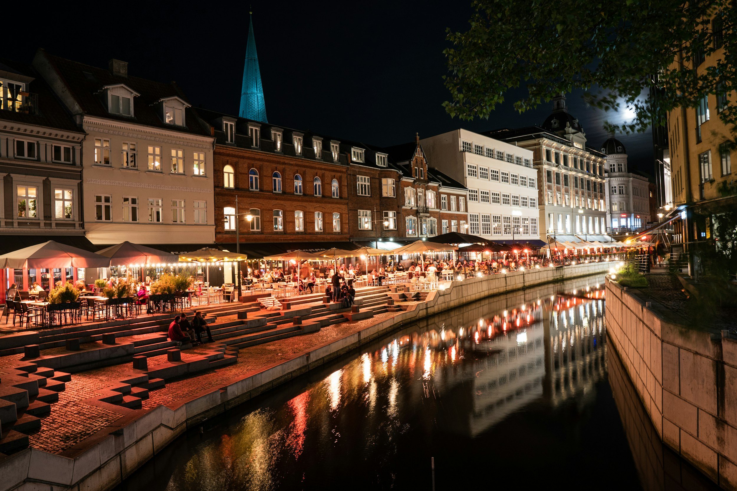Lively waterfront restaurants reflected in the canal at night in central Aarhus, Denmark.