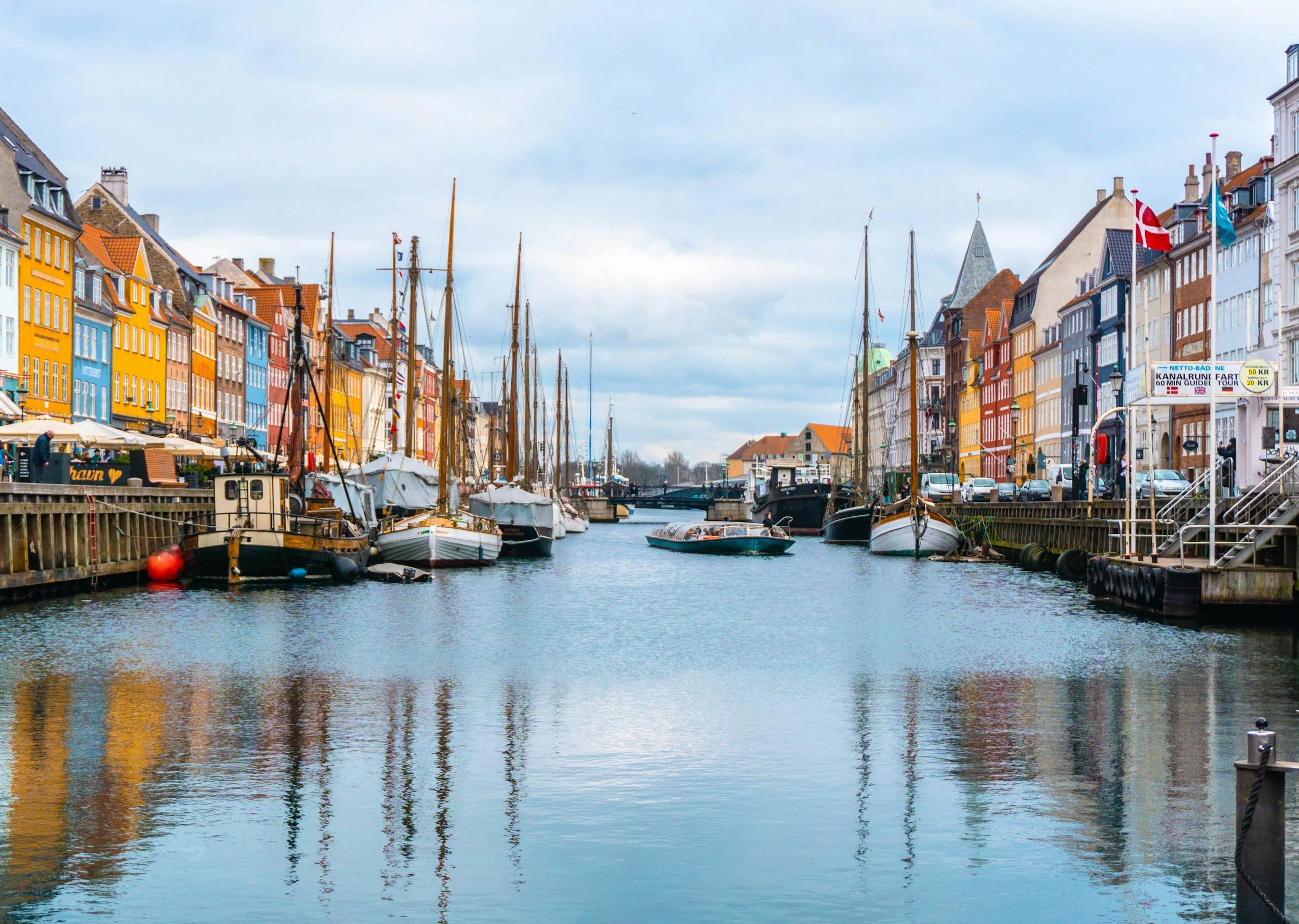 Historic sailing boats and colourful waterfront buildings lining Nyhavn harbour in Copenhagen, Denmark.