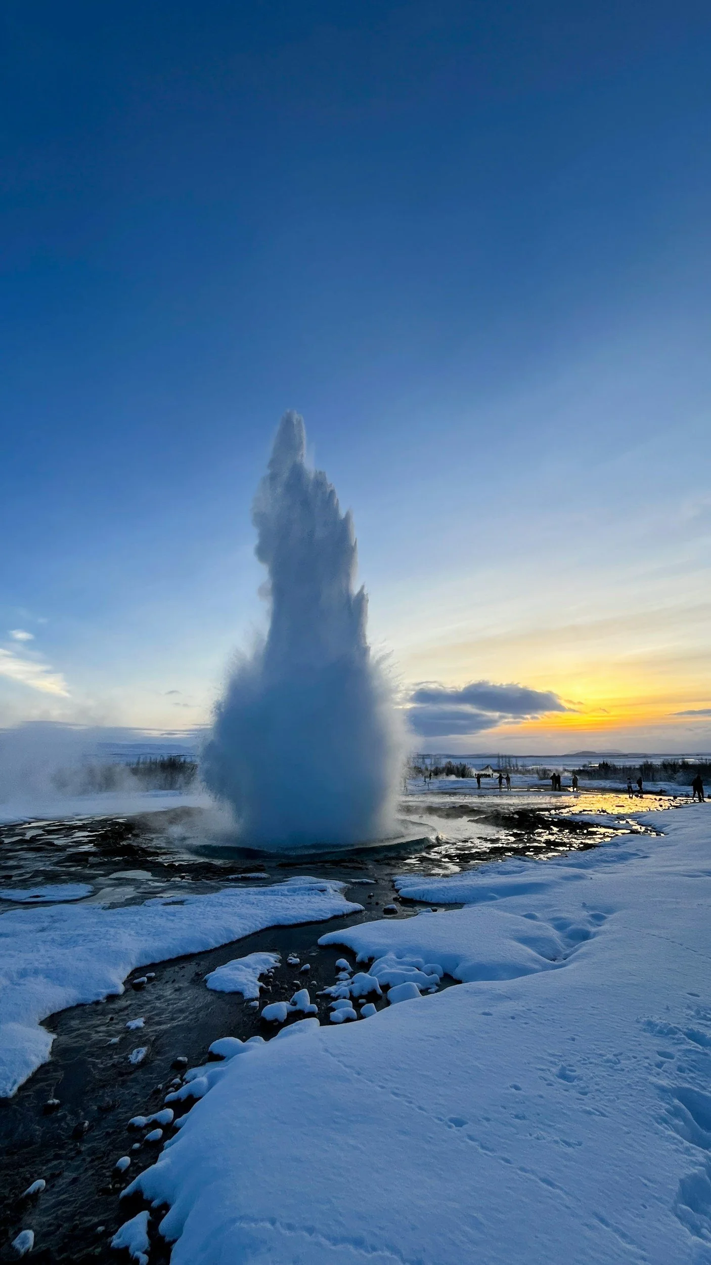Powerful geyser erupting from a snow-covered geothermal landscape at sunset in Iceland.