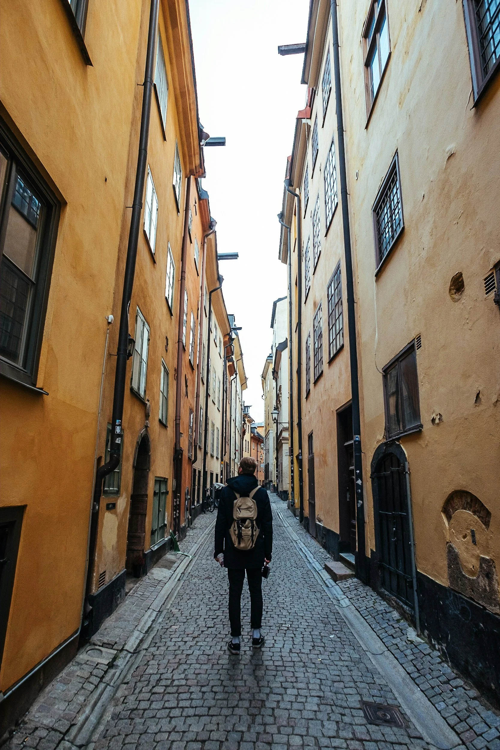 A traveller walks along a narrow cobblestone street lined with colourful historic buildings in Stockholm, Sweden.