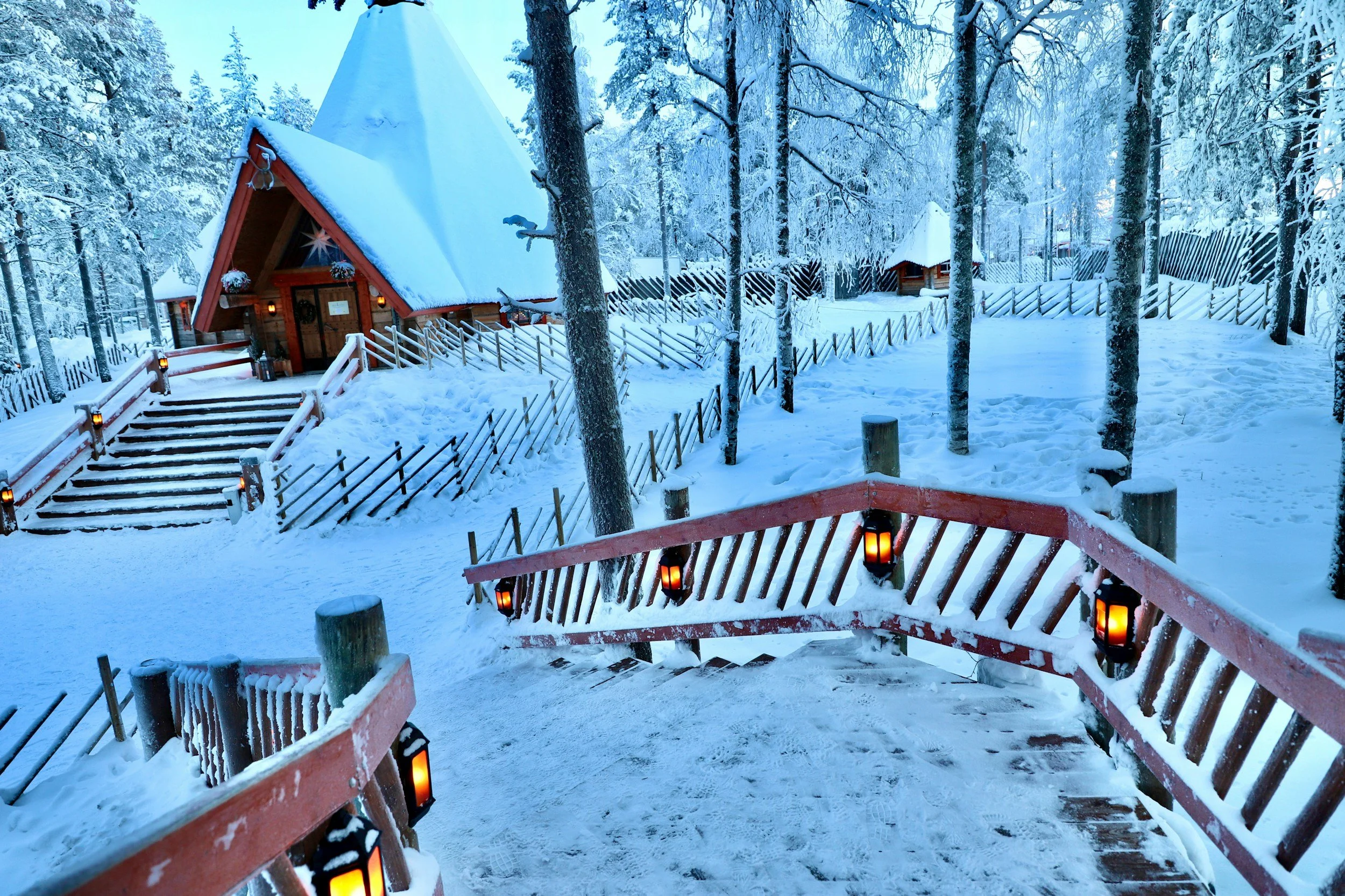 Snow-covered wooden cabins decorated with warm lights in a forest in Rovaniemi, Finnish Lapland.