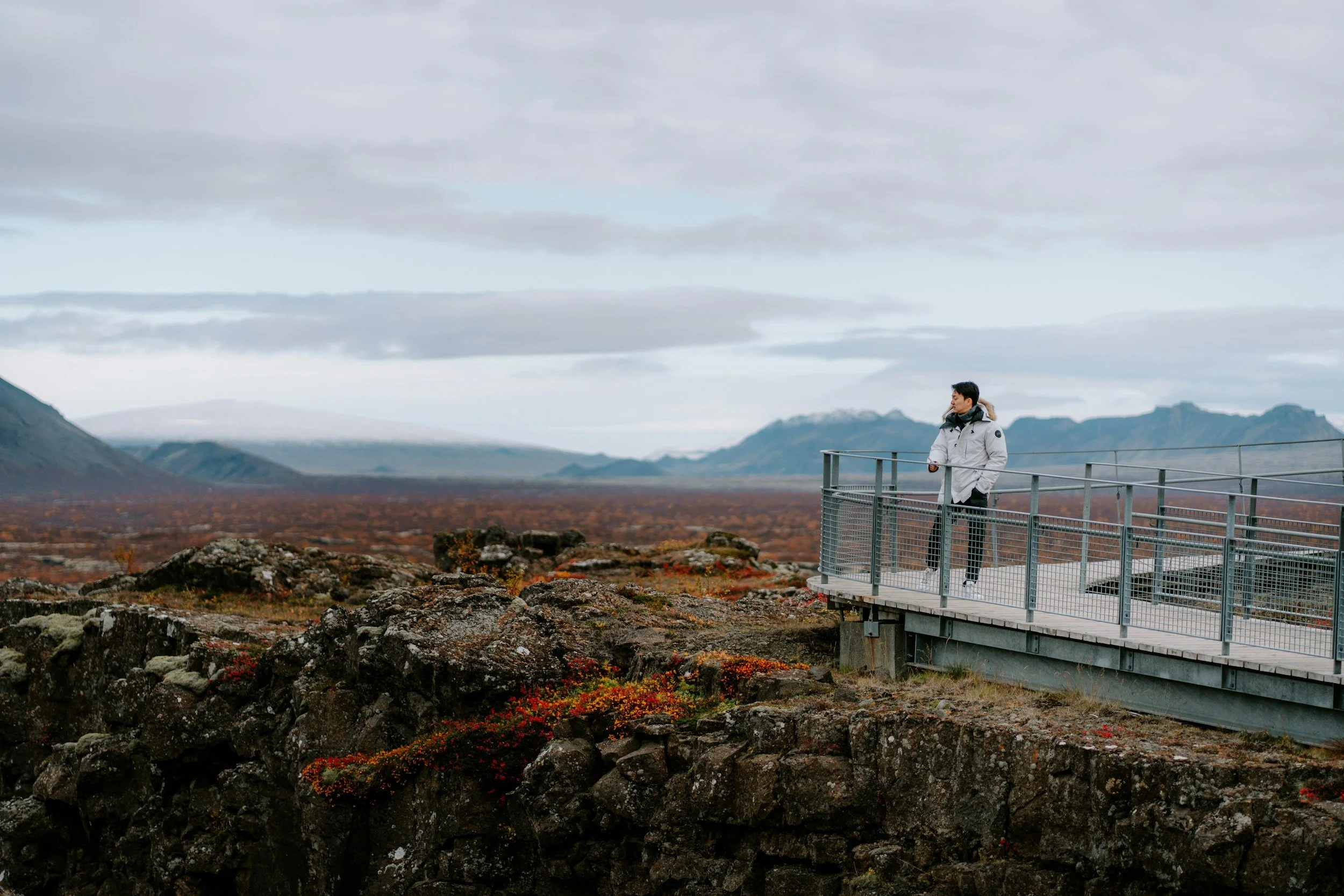 A traveller stands at a viewpoint overlooking the volcanic landscape and mountains of Þingvellir National Park.