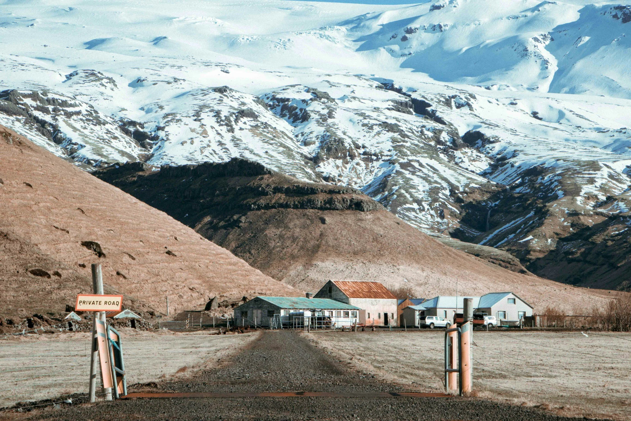 A remote farm surrounded by dramatic snow-covered mountains in rural Iceland.