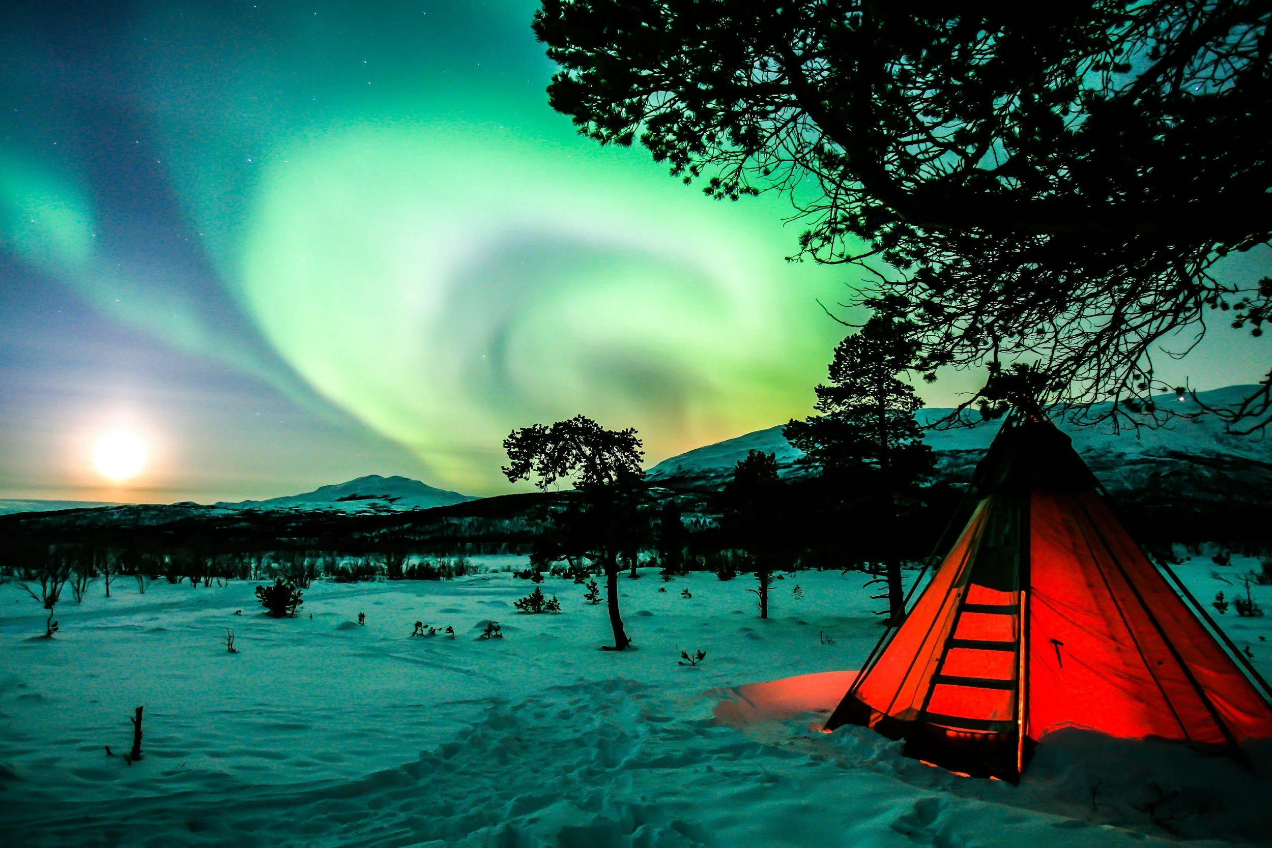 Green Northern Lights swirl above a glowing tent in the snowy landscape of Abisko, Swedish Lapland.
