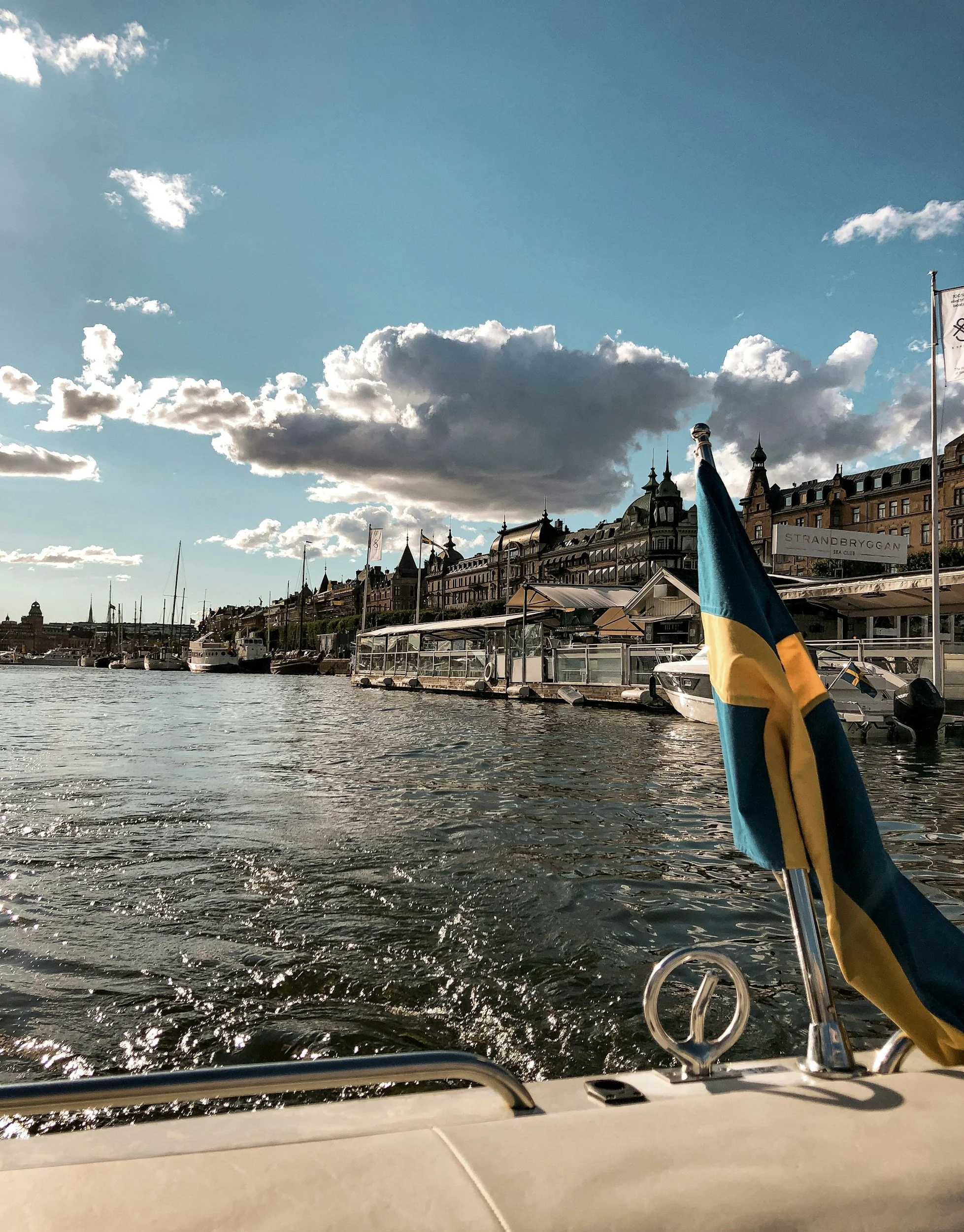View of Stockholm’s waterfront from a boat with a Swedish flag flying in the foreground.