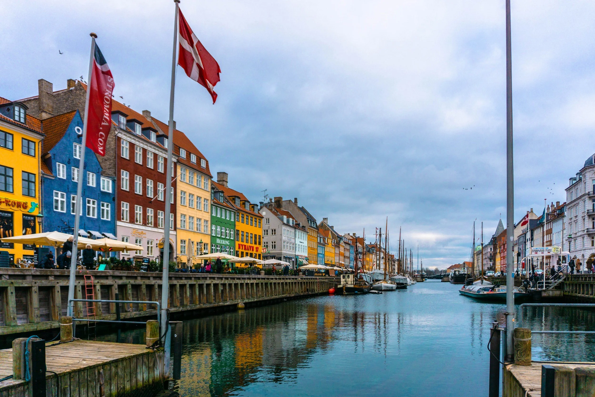 The Danish flag flies above colourful waterfront buildings and boats along Nyhavn canal in Copenhagen.