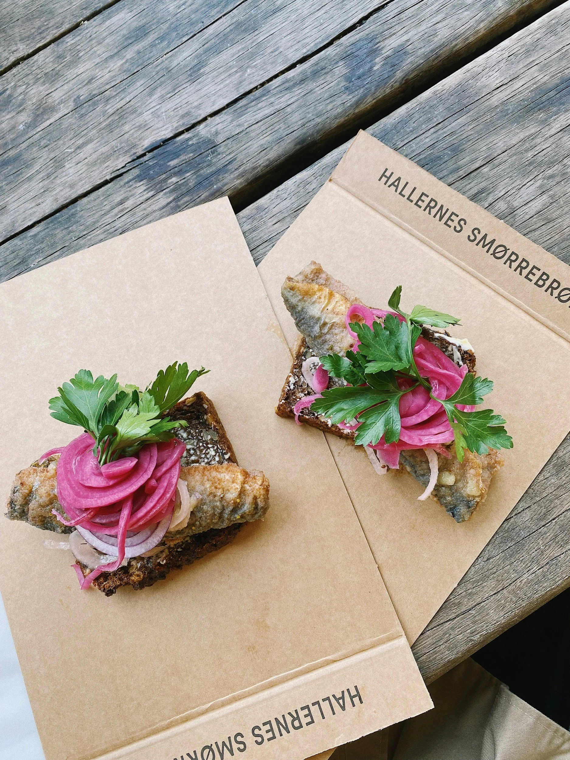 Two Danish smørrebrød open sandwiches topped with herring, pickled red onion and fresh herbs.
