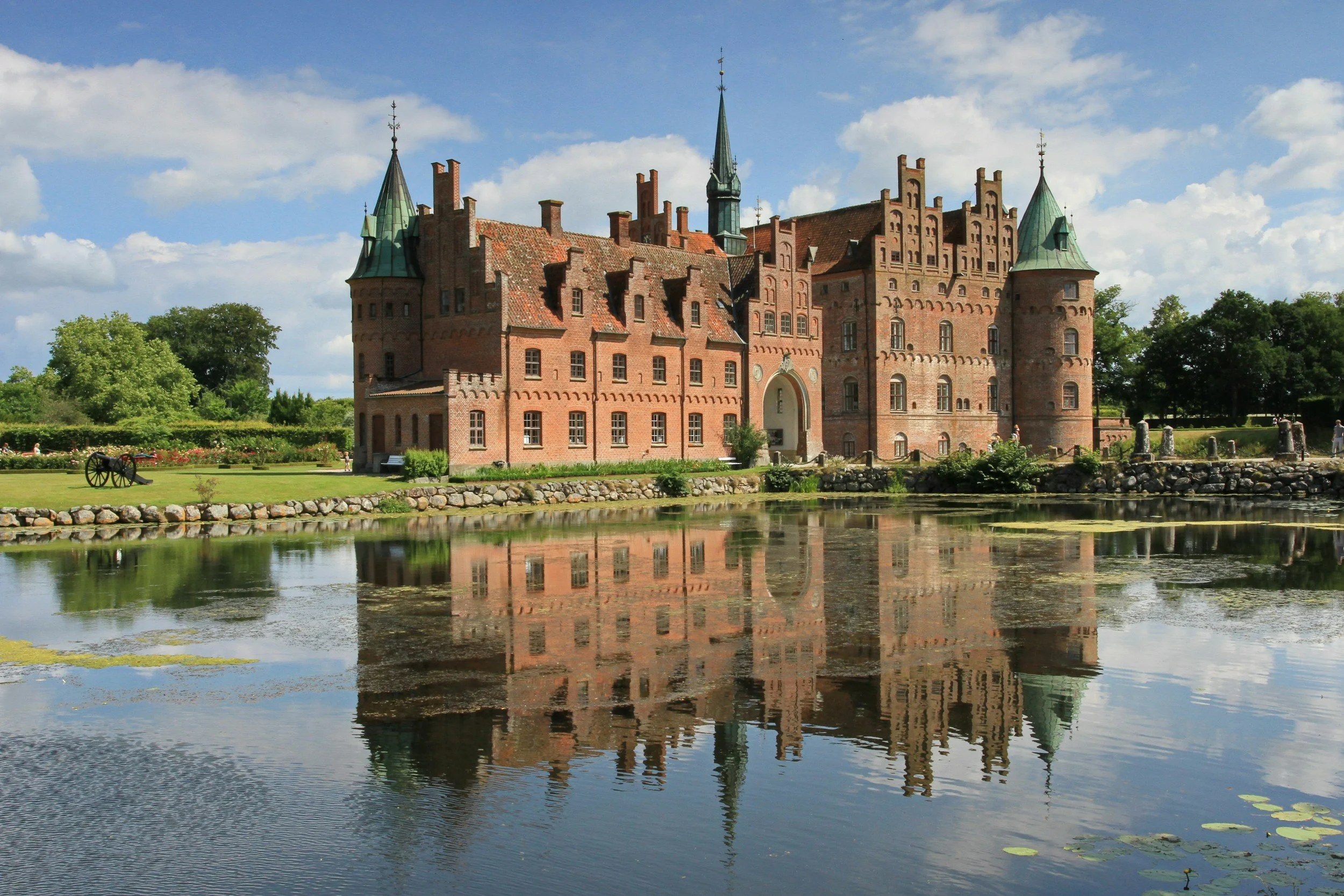 Egeskov Castle reflected in the surrounding water beneath a blue summer sky in Denmark.
