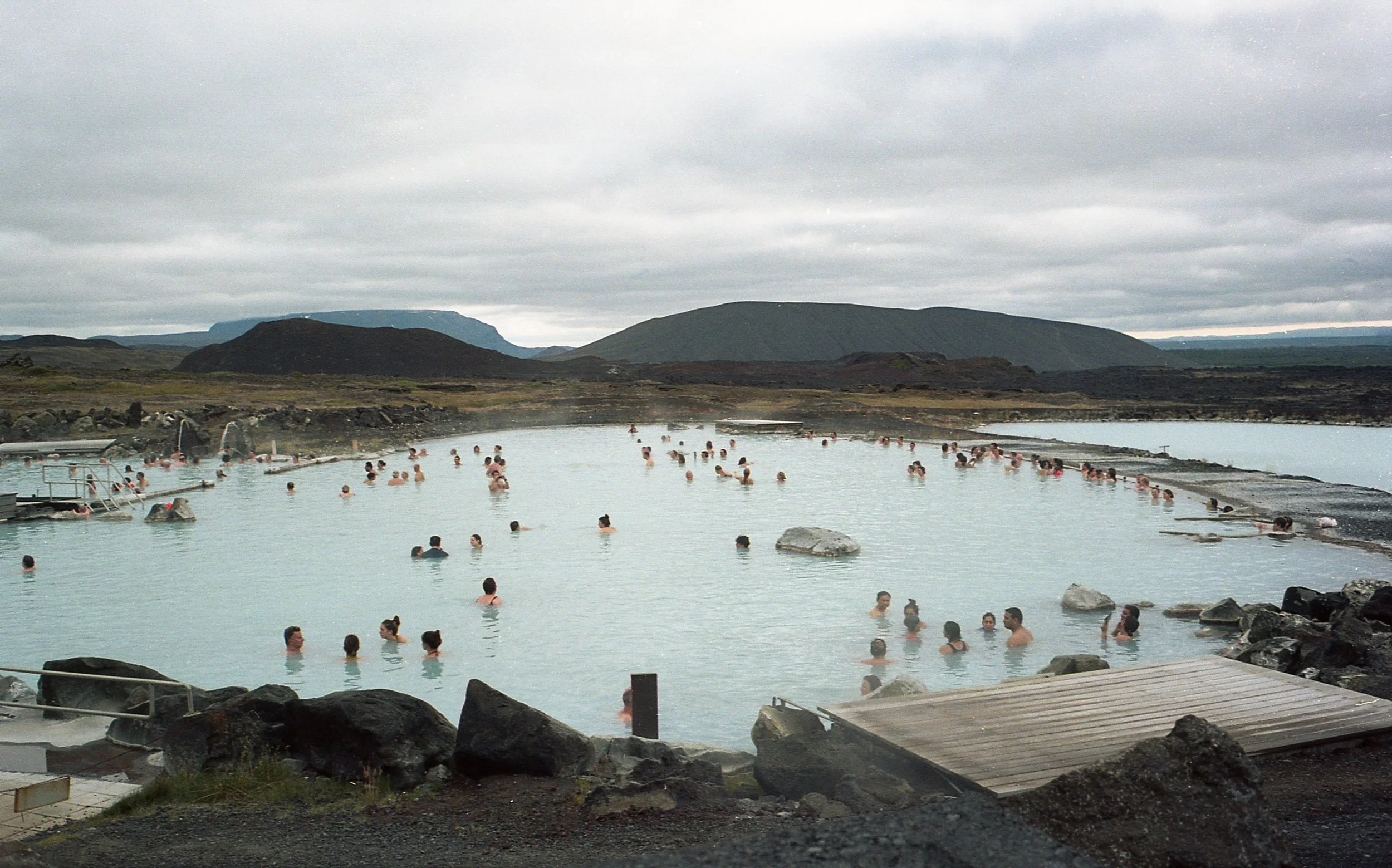 Visitors relax in a steaming geothermal lagoon surrounded by dark volcanic scenery in Iceland.