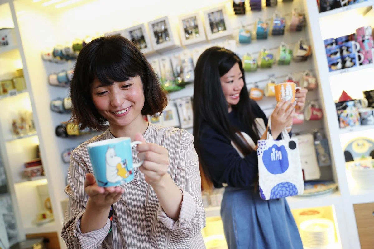 Two visitors browse colourful Moomin mugs and souvenirs in a shop in Helsinki, Finland.
