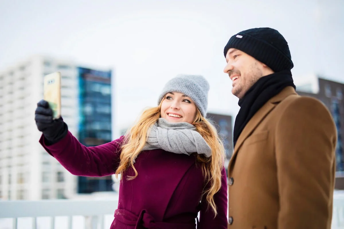 A couple wearing warm winter clothing take a selfie outdoors in snowy Oulu, Finland.