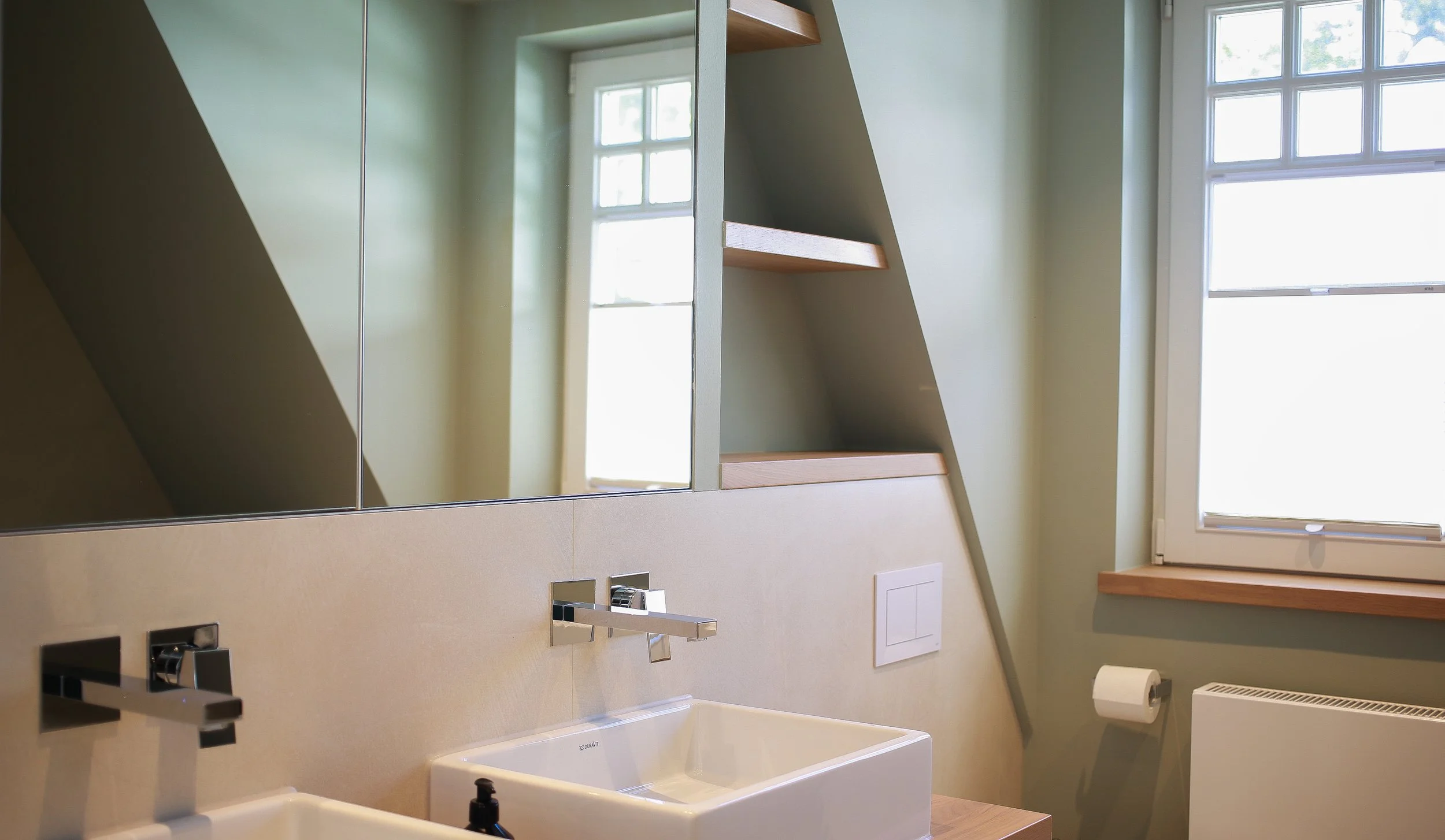 Badezimmer unter der Dachschräge mit gedecktem Grün-Grau, Naturstein und Holzdetails – abgestimmtes Farb- und Materialkonzept.